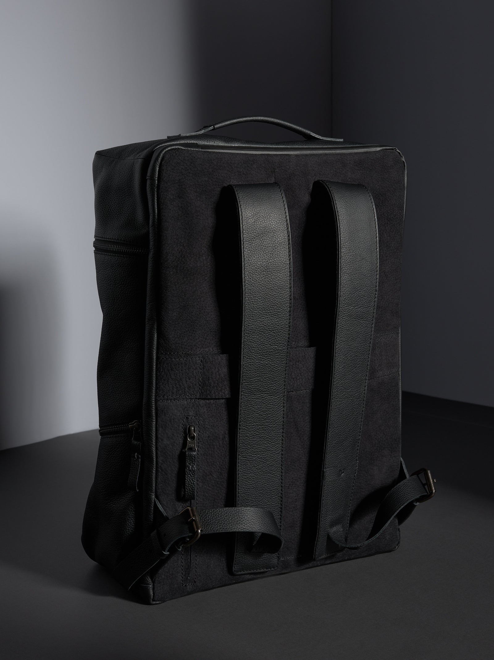 Back view of the black leather backpack showing the cushioned straps and premium suede-like backing for comfort.