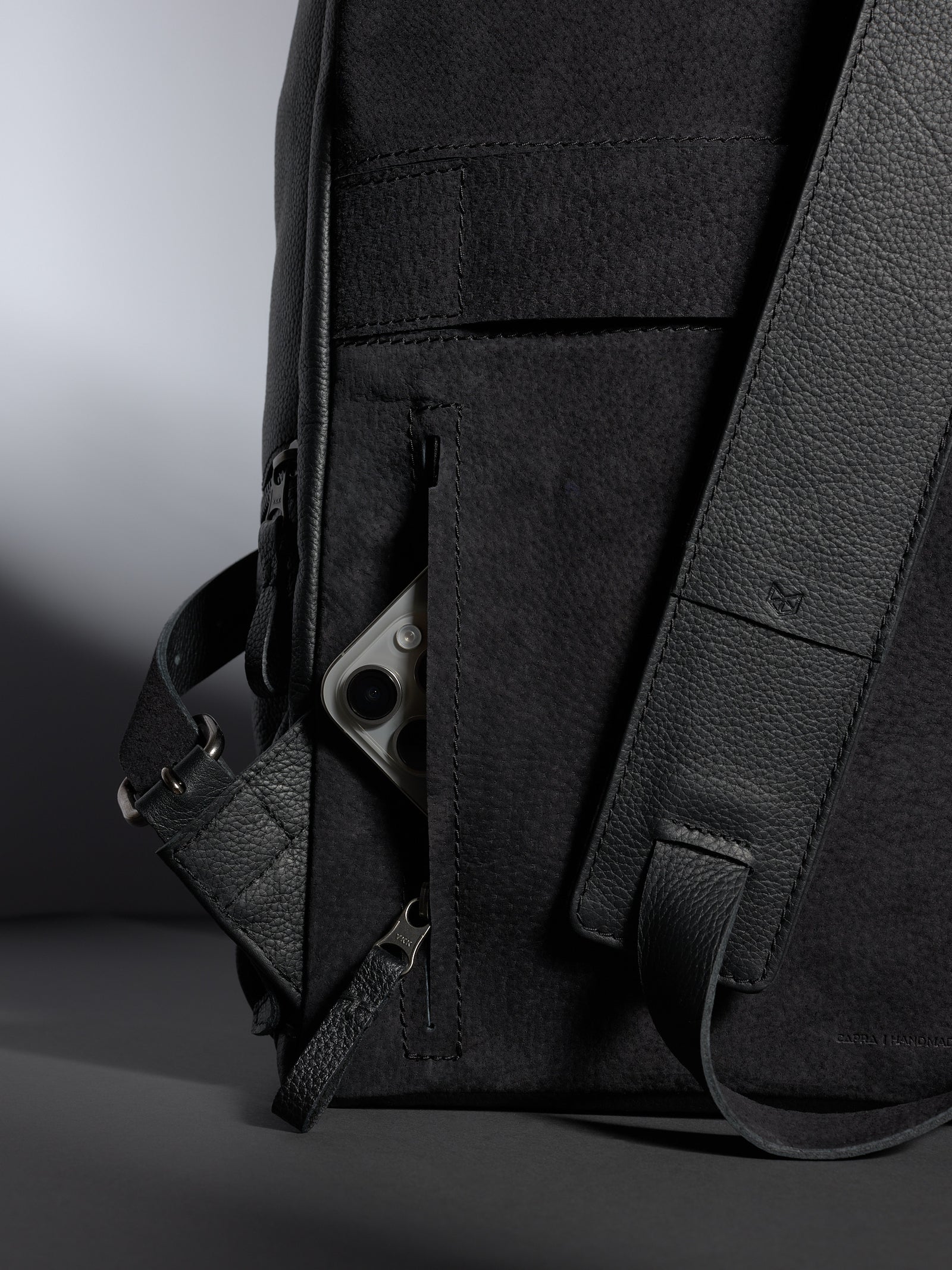 Capra-Leather-4.jpg Side-view close-up showing a smartphone tucked into a discreet, zippered back security pocket on a leather backpack.