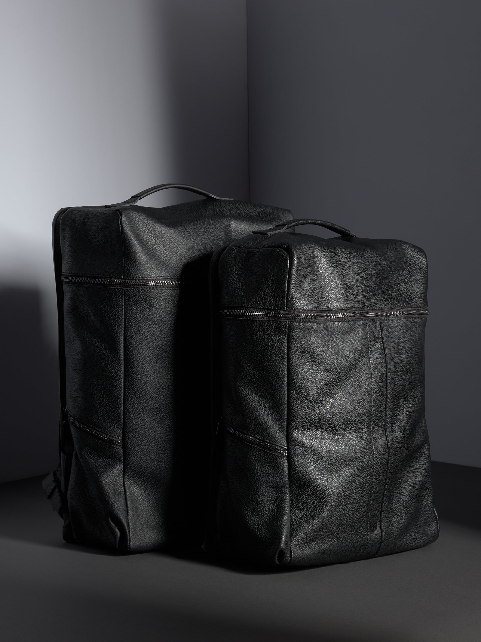 The large and smaller sizes of the Banteng black full-grain leather backpacks standing side-by-side.