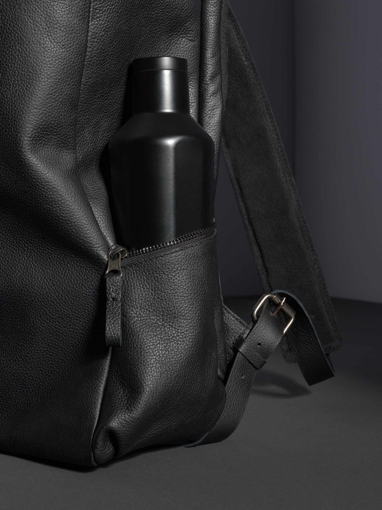 Black Capra Leather backpack's zippered side pocket with a matte black water bottle inserted.