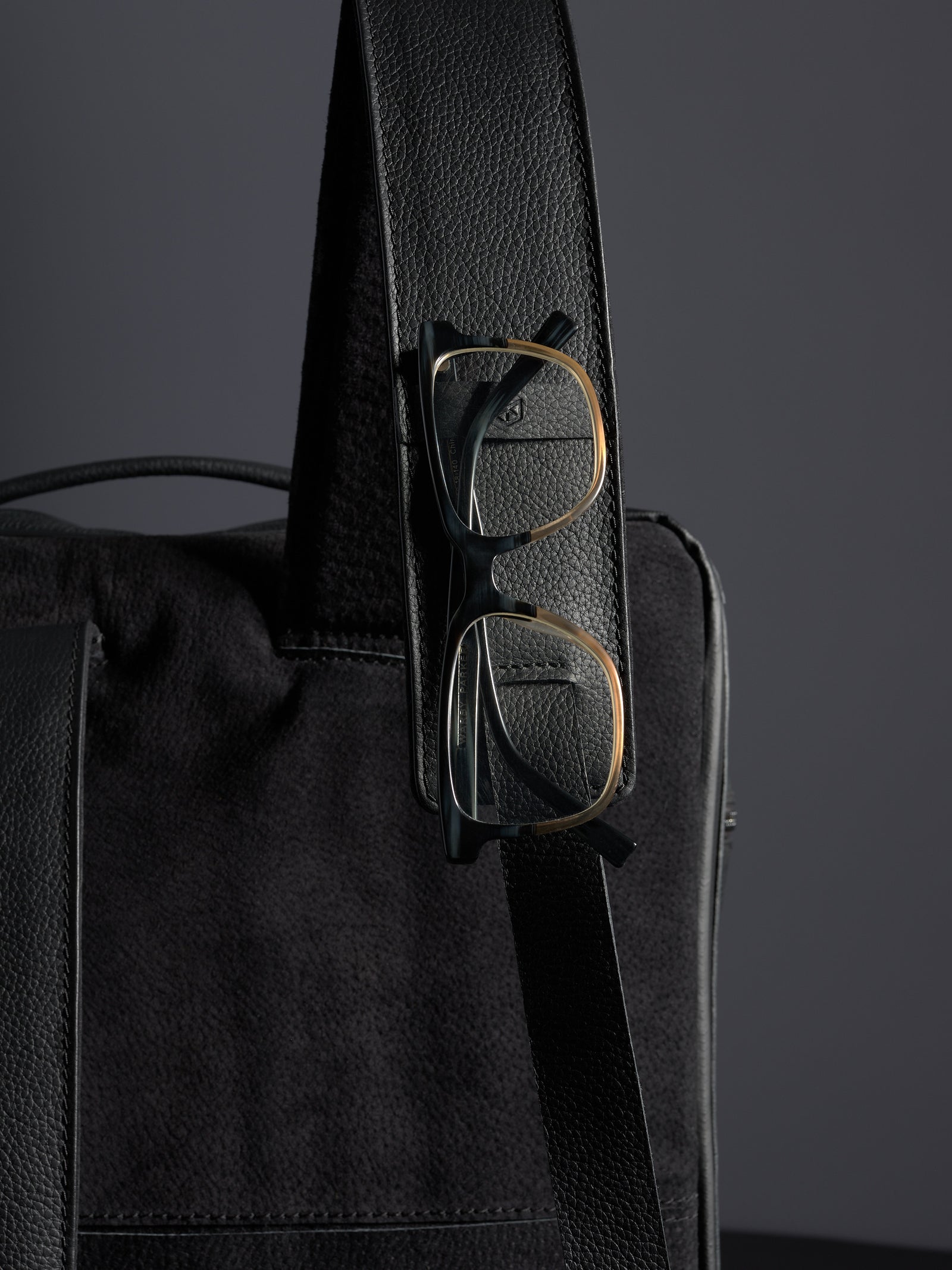 Close-up of Capra Leather black full-grain leather backpack strap with gold and black eyeglasses clipped on.