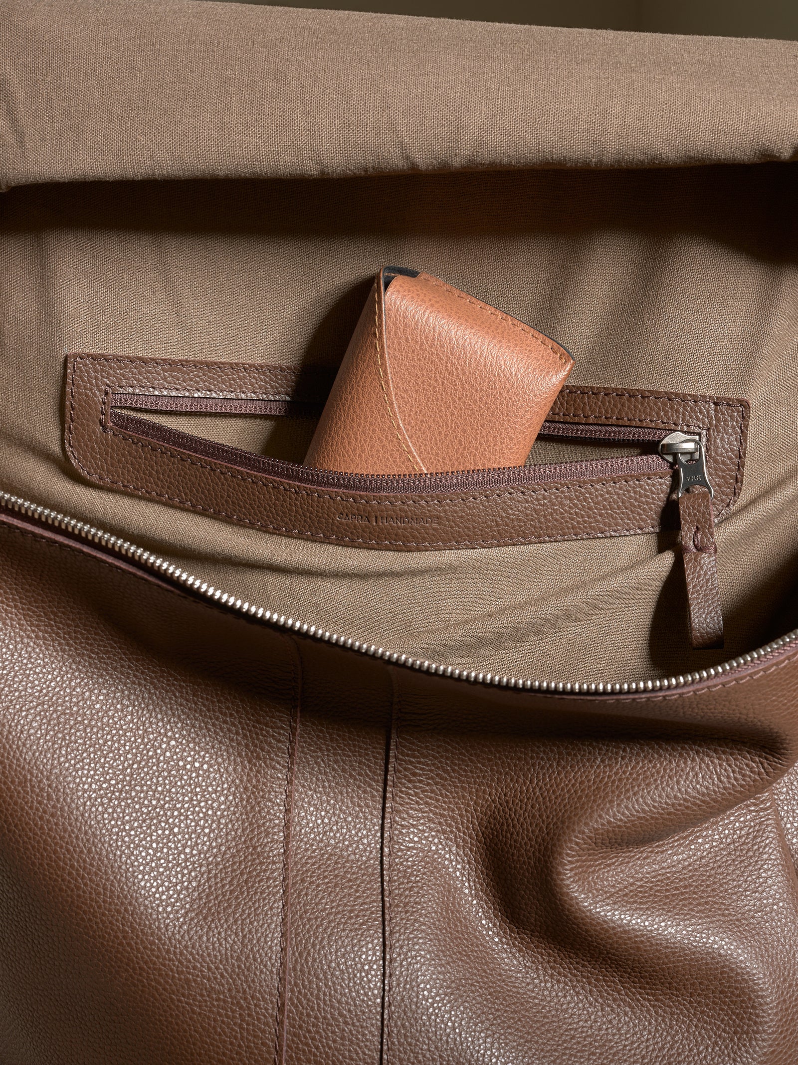 Interior shot of the Capra Leather backpack's lining with a zippered pocket holding a small leather wallet.