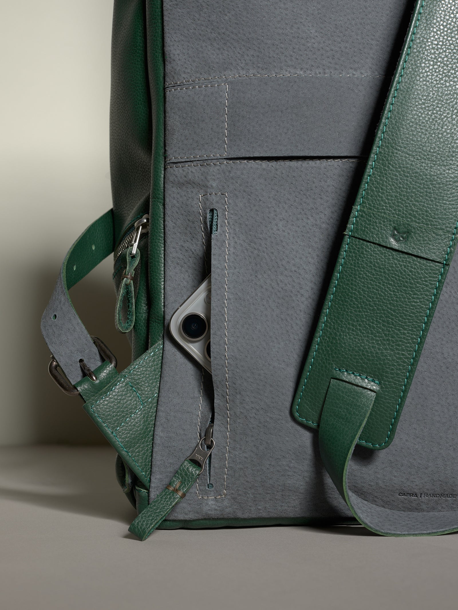 Back panel of the Capra Banteng leather backpack in green and gray with a hidden pocket storing a cell phone.