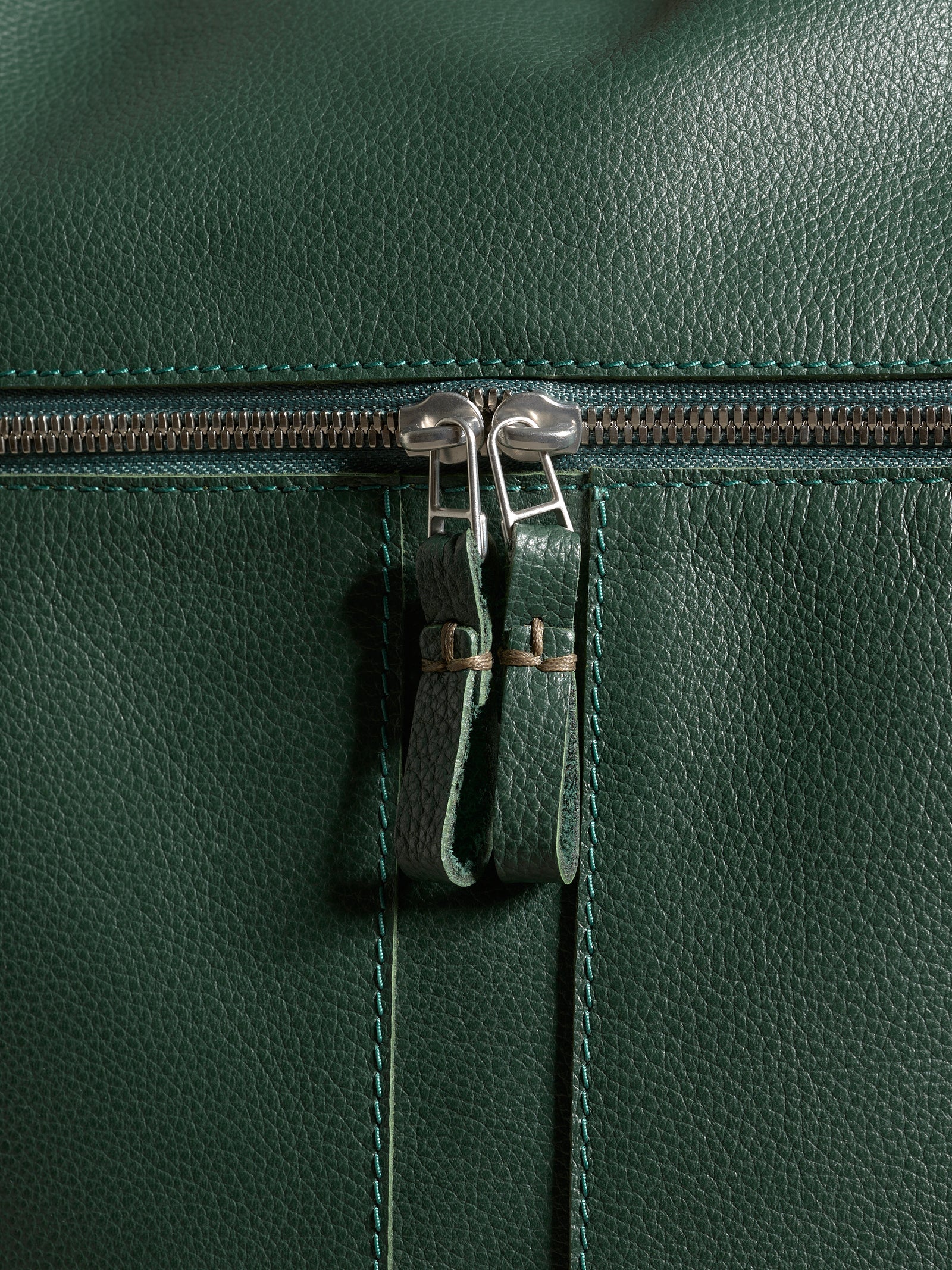 Close-up of the durable metal dual zippers and detailed stitching on the pebbled green leather Banteng backpack.