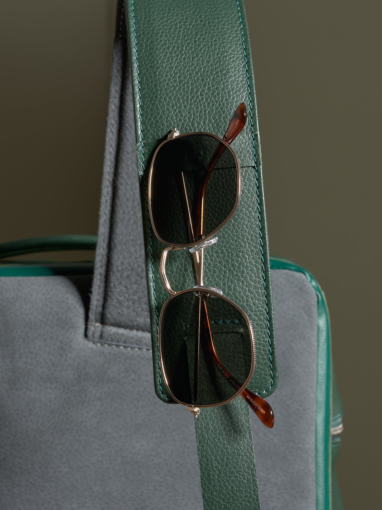 Green leather shoulder strap detail on the Banteng backpack, featuring a functional loop holding a pair of sunglasses.
