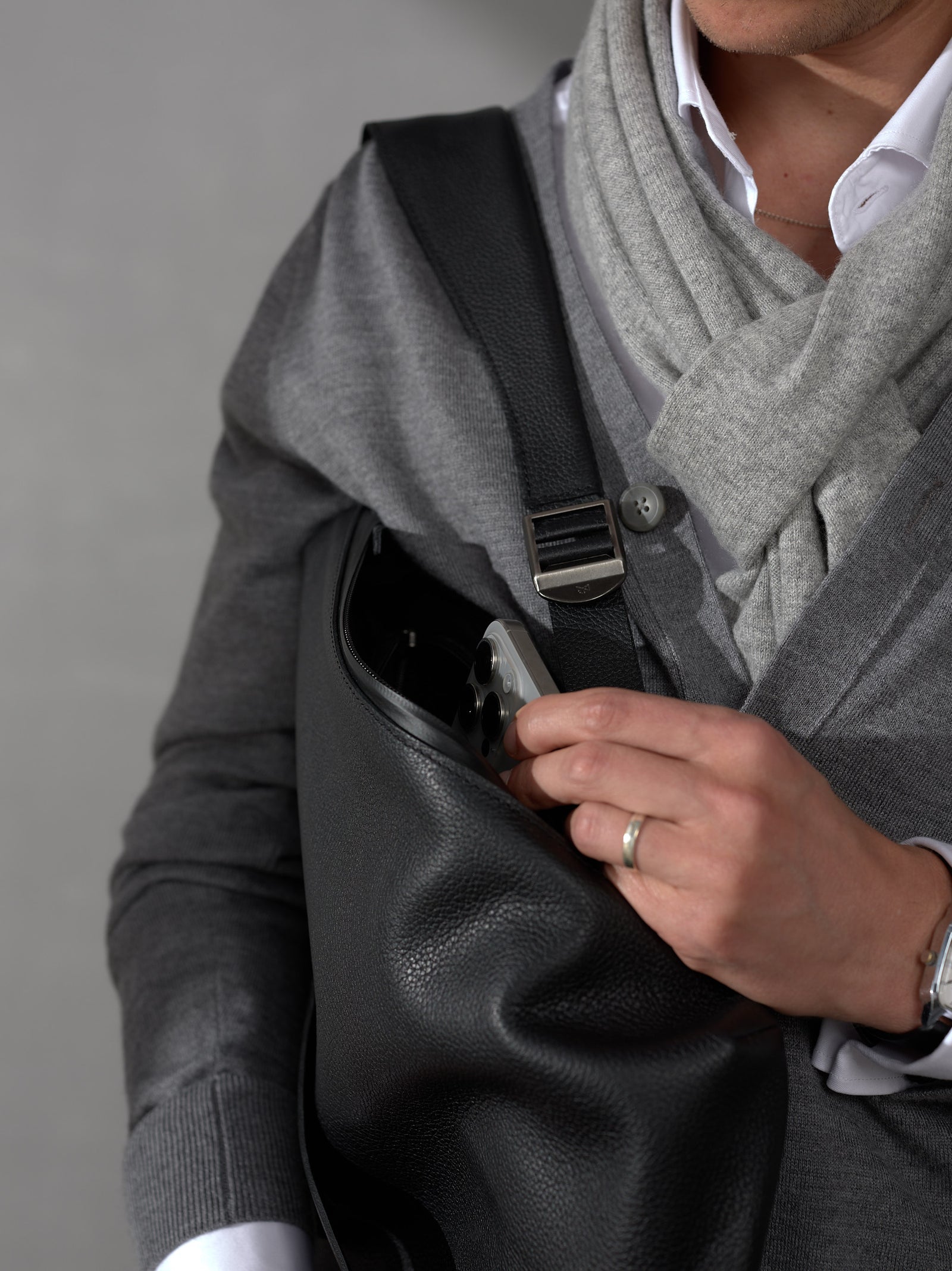 Close-up of a man sliding a smartphone into the easily accessible side pocket of a black leather travel backpack.