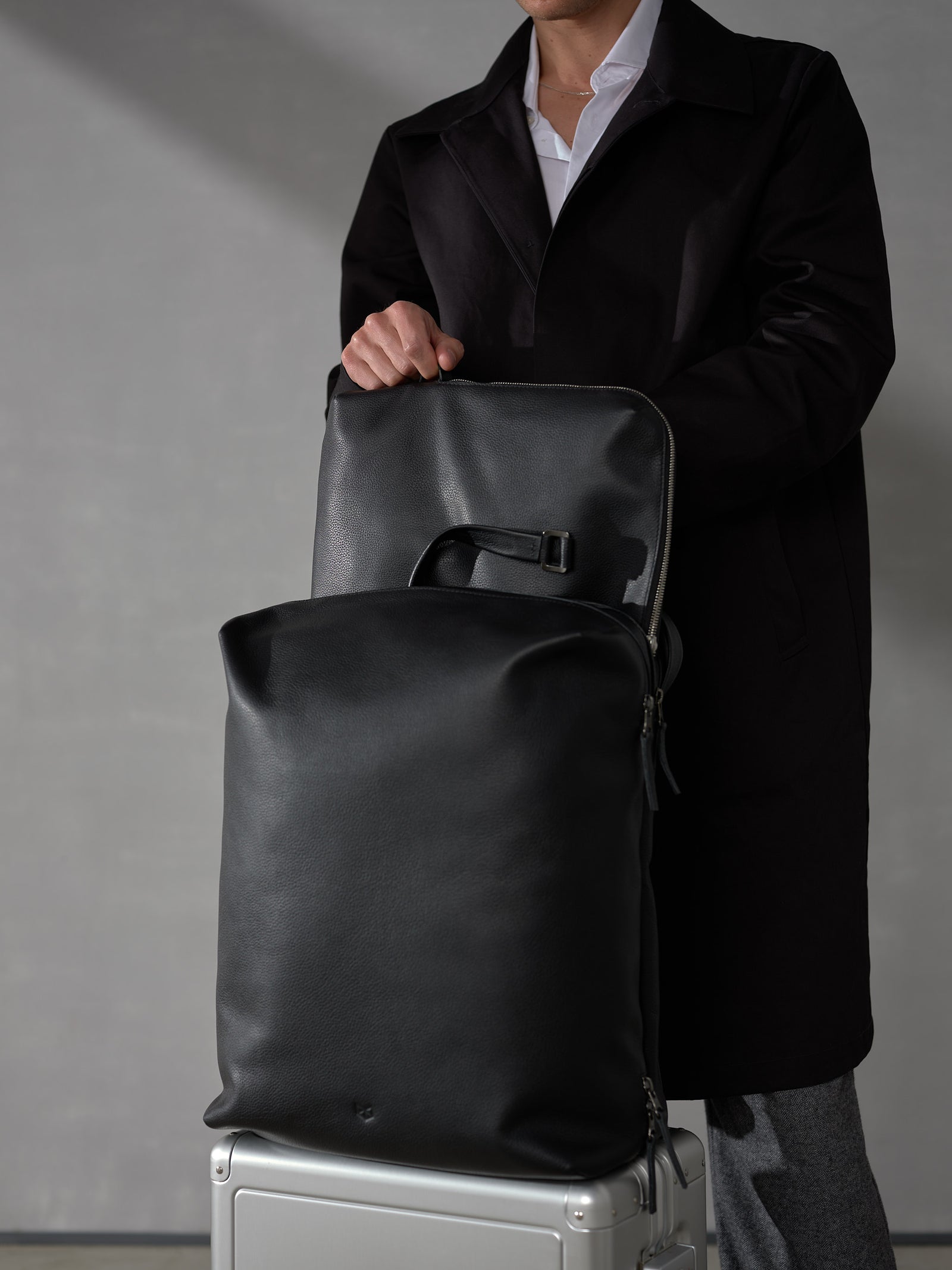Close-up of a man extracting a matching black leather laptop sleeve from a premium travel backpack.