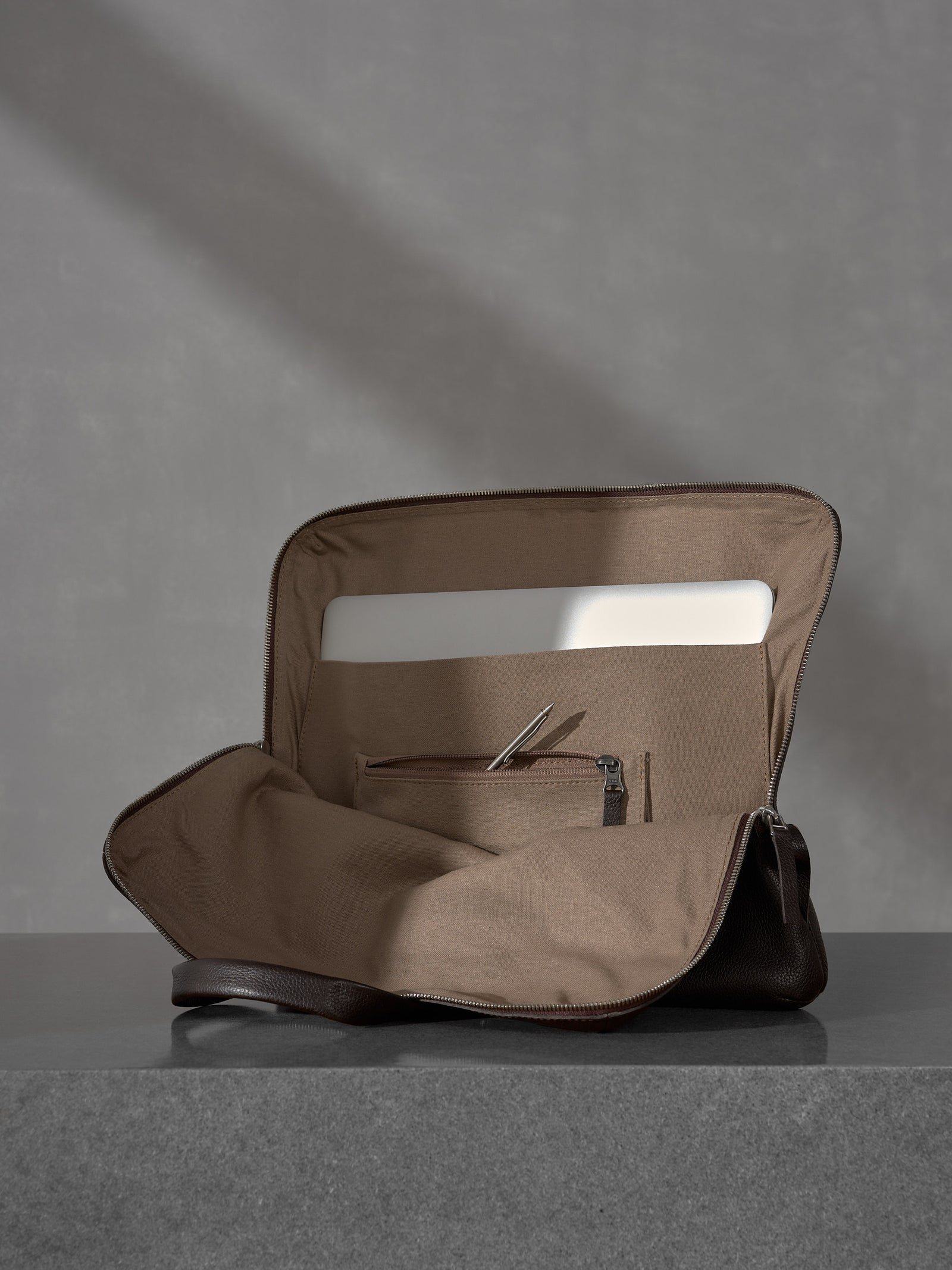 Open Capra Leather briefcase showing a laptop compartment and zippered pocket with a pen.