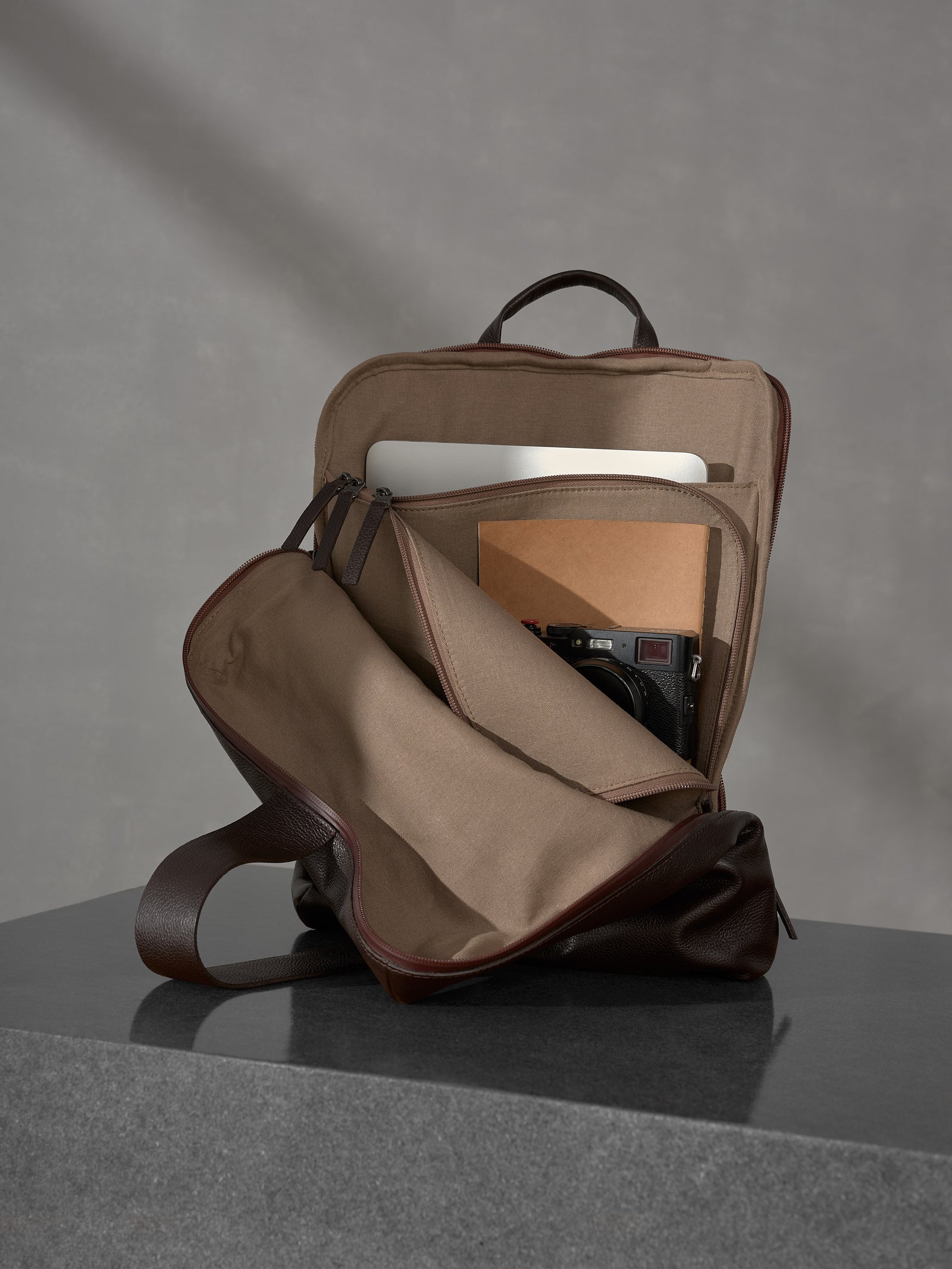 Open Capra Leather backpack revealing a laptop, notebook, and mirrorless camera packed inside.