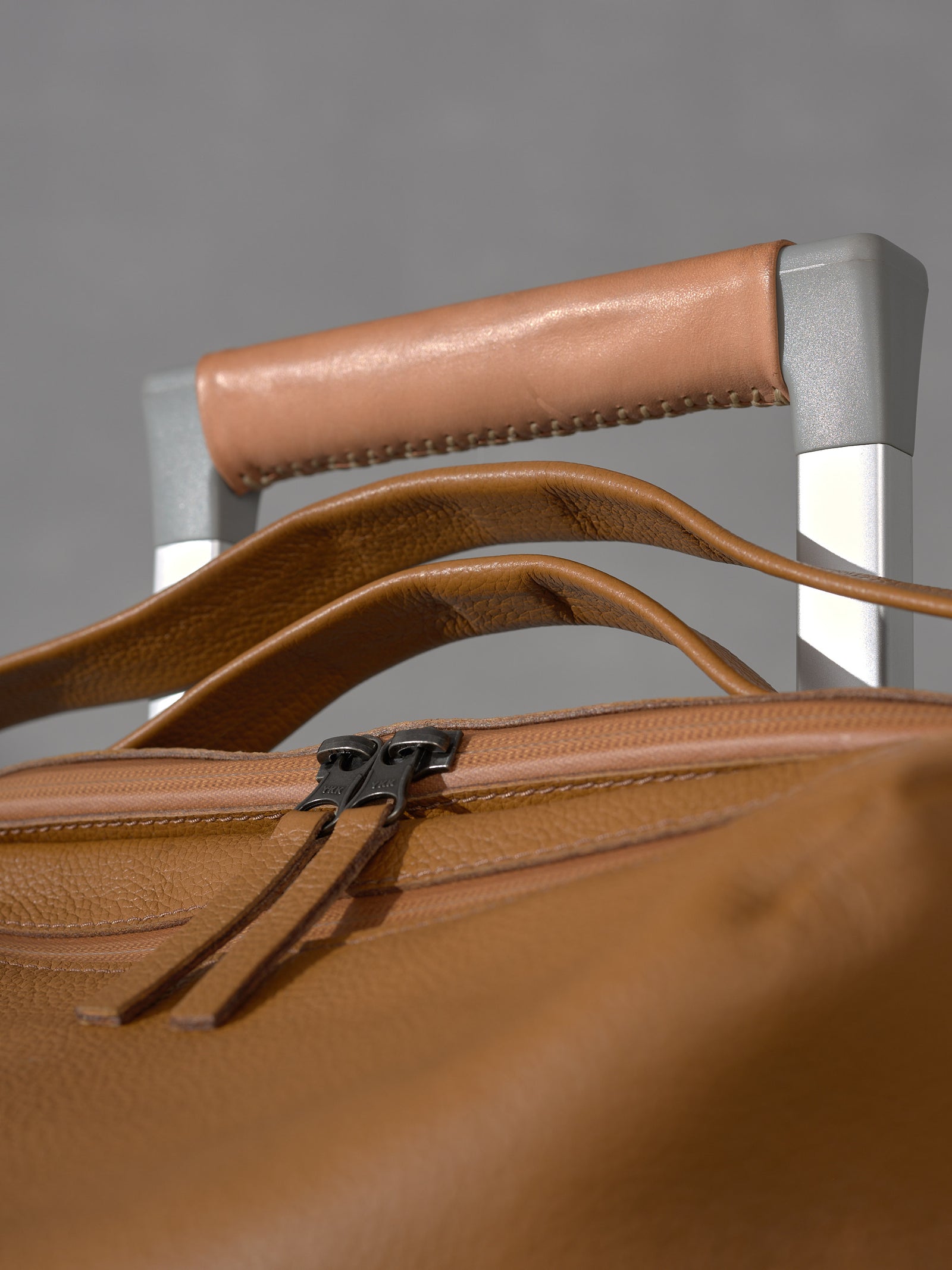 Close-up of the premium leather craftsmanship on the Basalt carry-on system bag, highlighting the stitched tan leather handle wrap, sturdy zippers, and silver hardware.