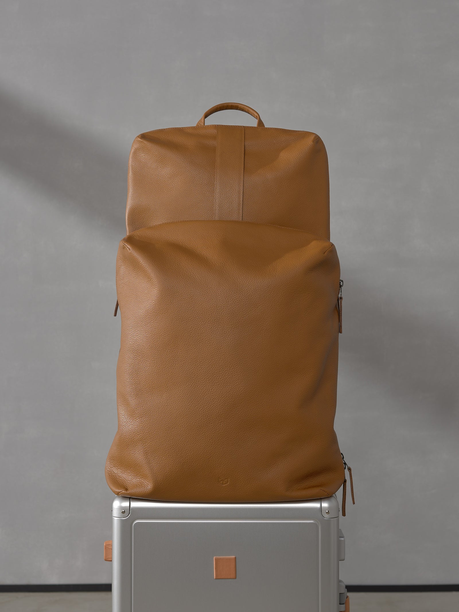 Front view of two modular tan full-grain leather bags from the Capra Leather Basalt system securely stacked on top of a silver rolling suitcase.