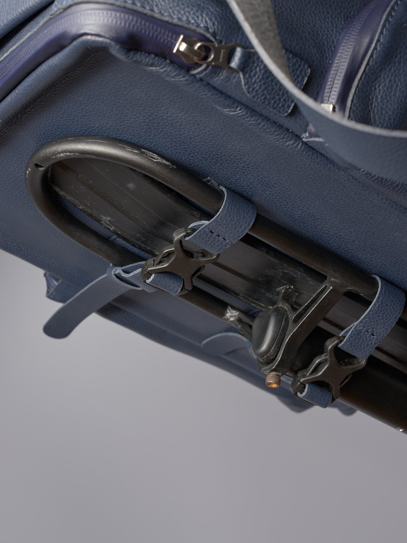 Underside of the blue leather bike bag showing the quick-release rack attachment system and leather securing straps.