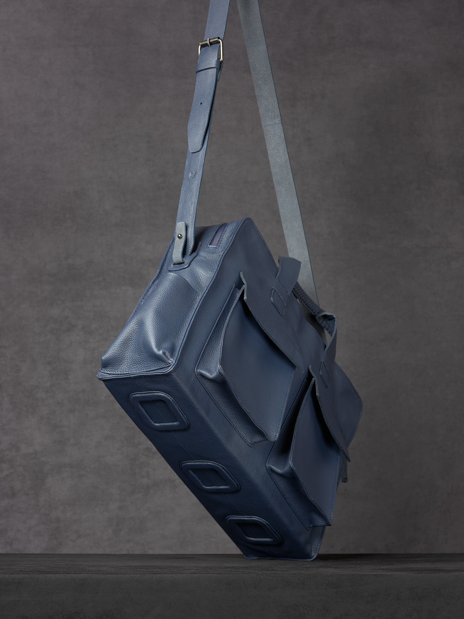 Floating view of Capra Leather navy leather messenger bag showing bottom panels.