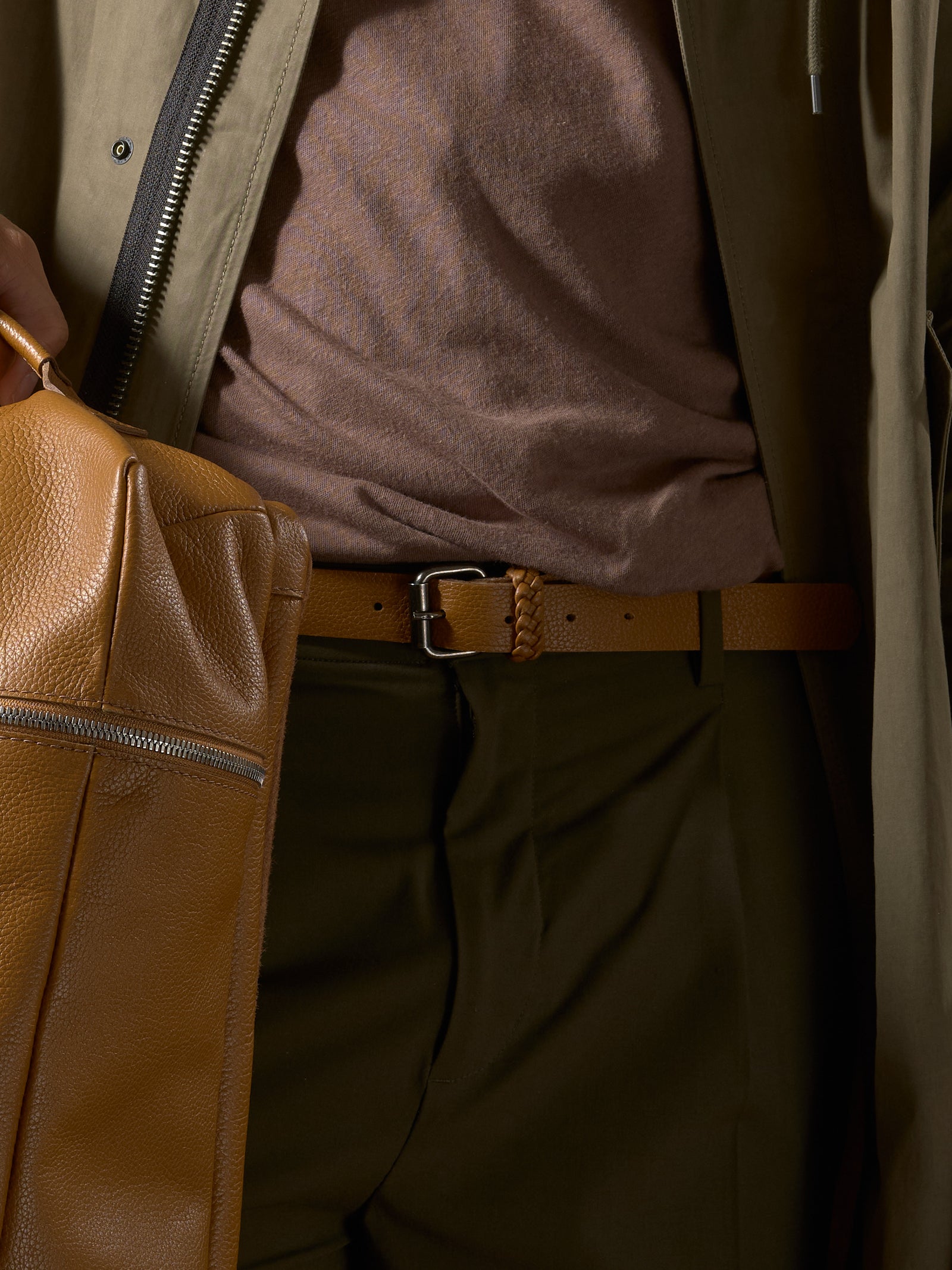 A man's torso showcasing a braided Capra Leather belt, olive green pants, and a tan leather bag.