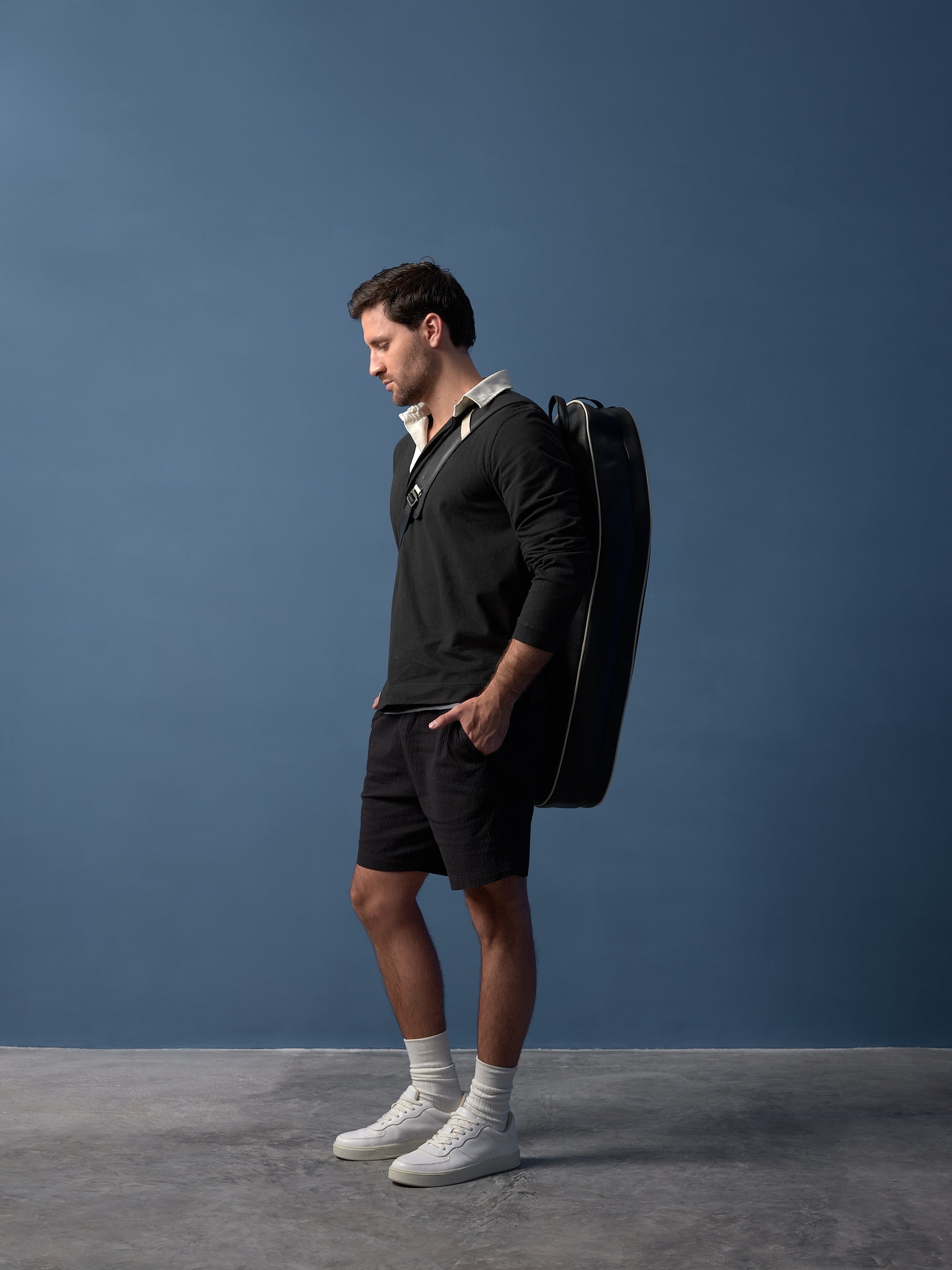 Side profile of a man carrying a slim, elegant black leather tennis bag as a backpack.