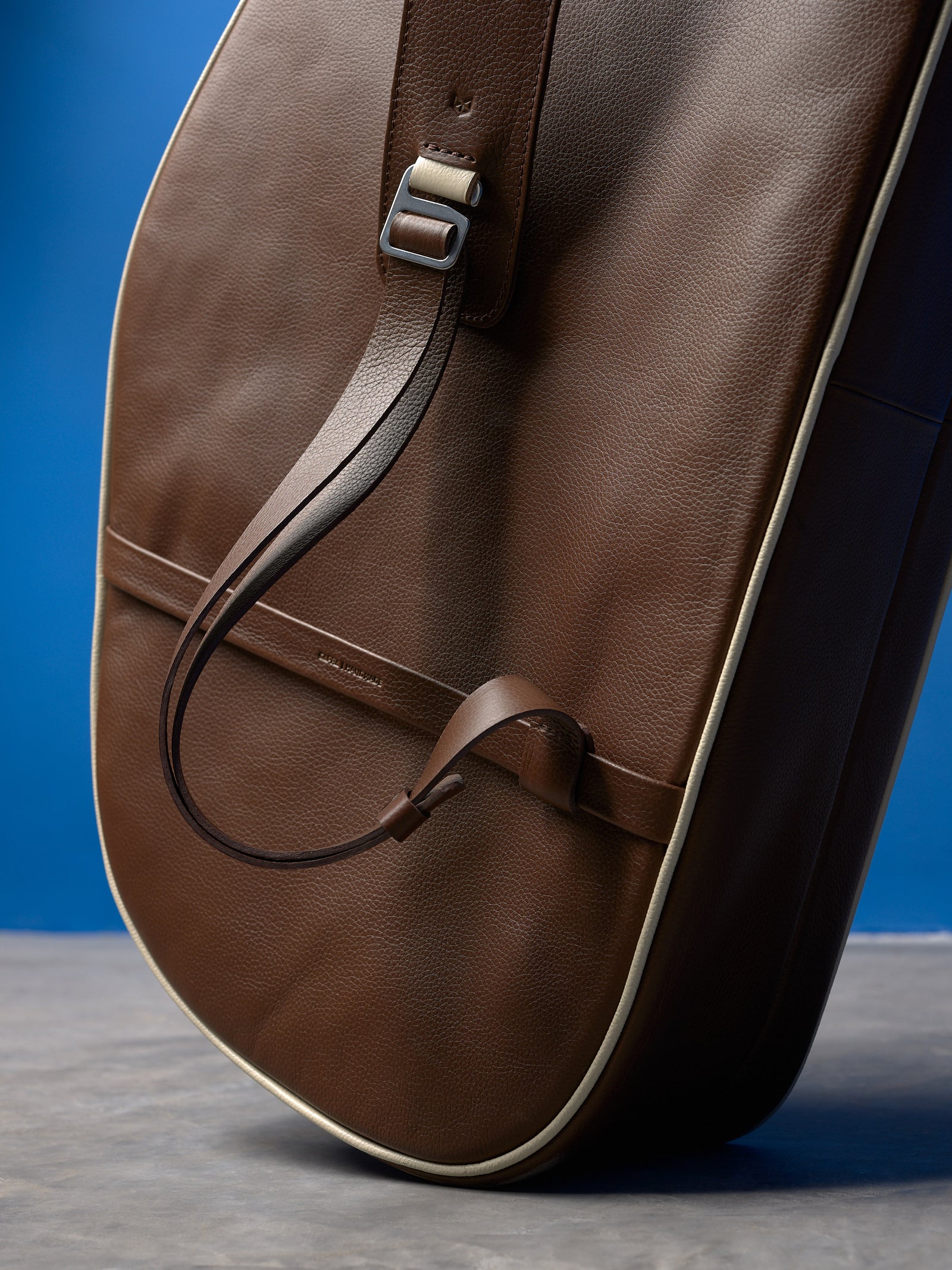 Detail of the adjustable brown leather strap on a tennis bag, featuring a metal buckle and cream leather accents.