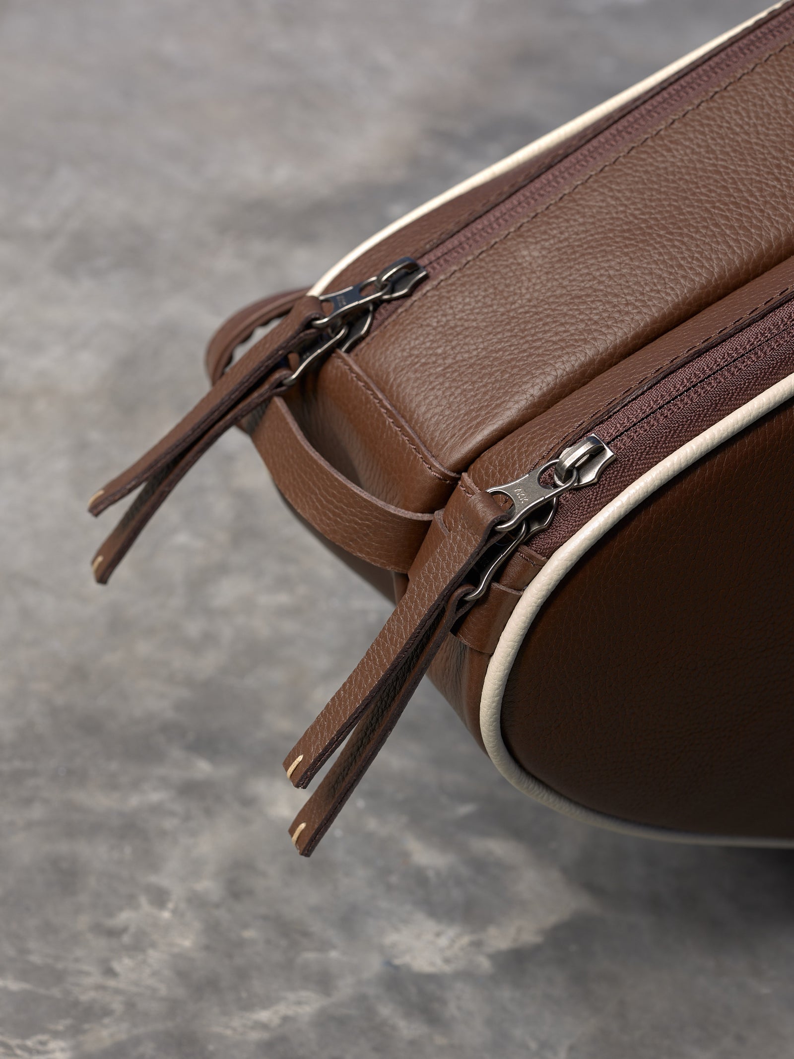 Macro shot of the high-quality YKK zippers with leather pulls on a brown leather tennis racket bag.