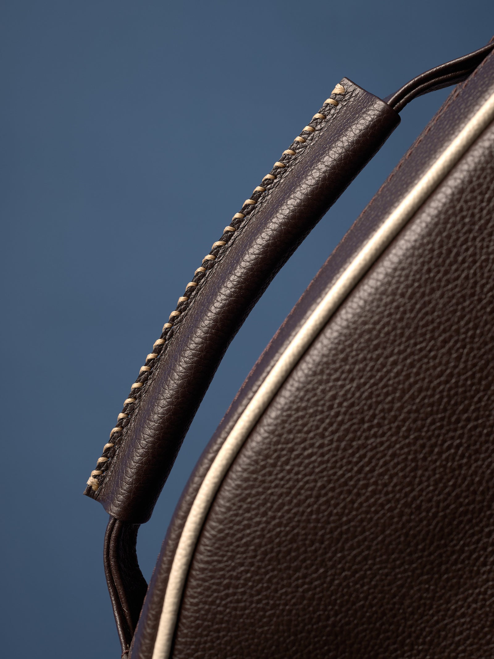 Close-up detail of a dark brown leather handle with cream-colored contrast stitching, showing the premium leather grain.