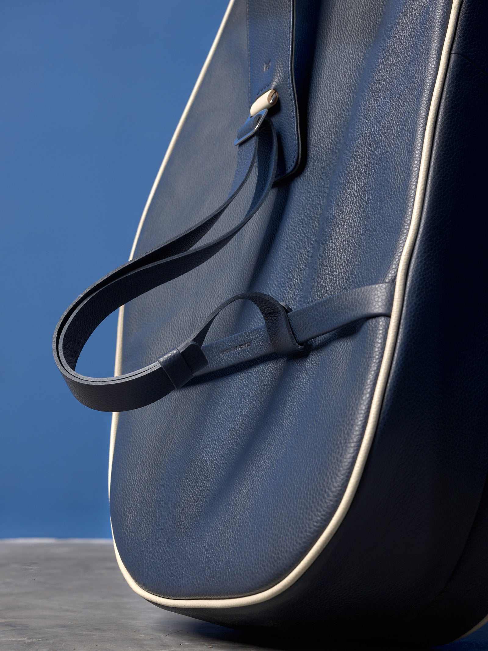 Detail of the leather strap loop on the navy blue tennis bag, showing the precise cream stitching.