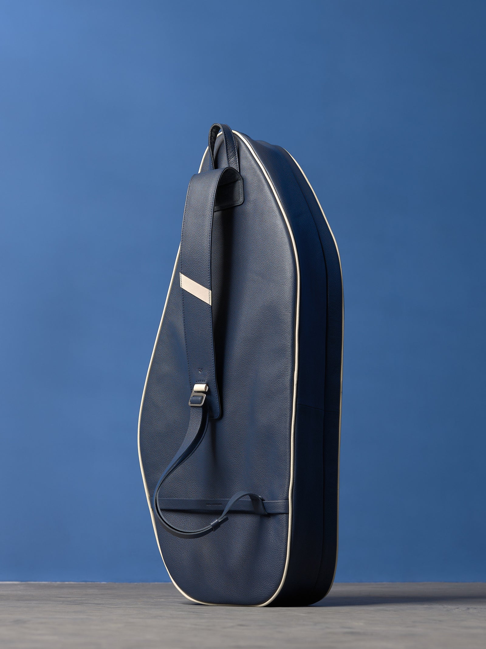 Navy blue full-grain leather tennis racket bag with white piping and a wide adjustable shoulder strap.