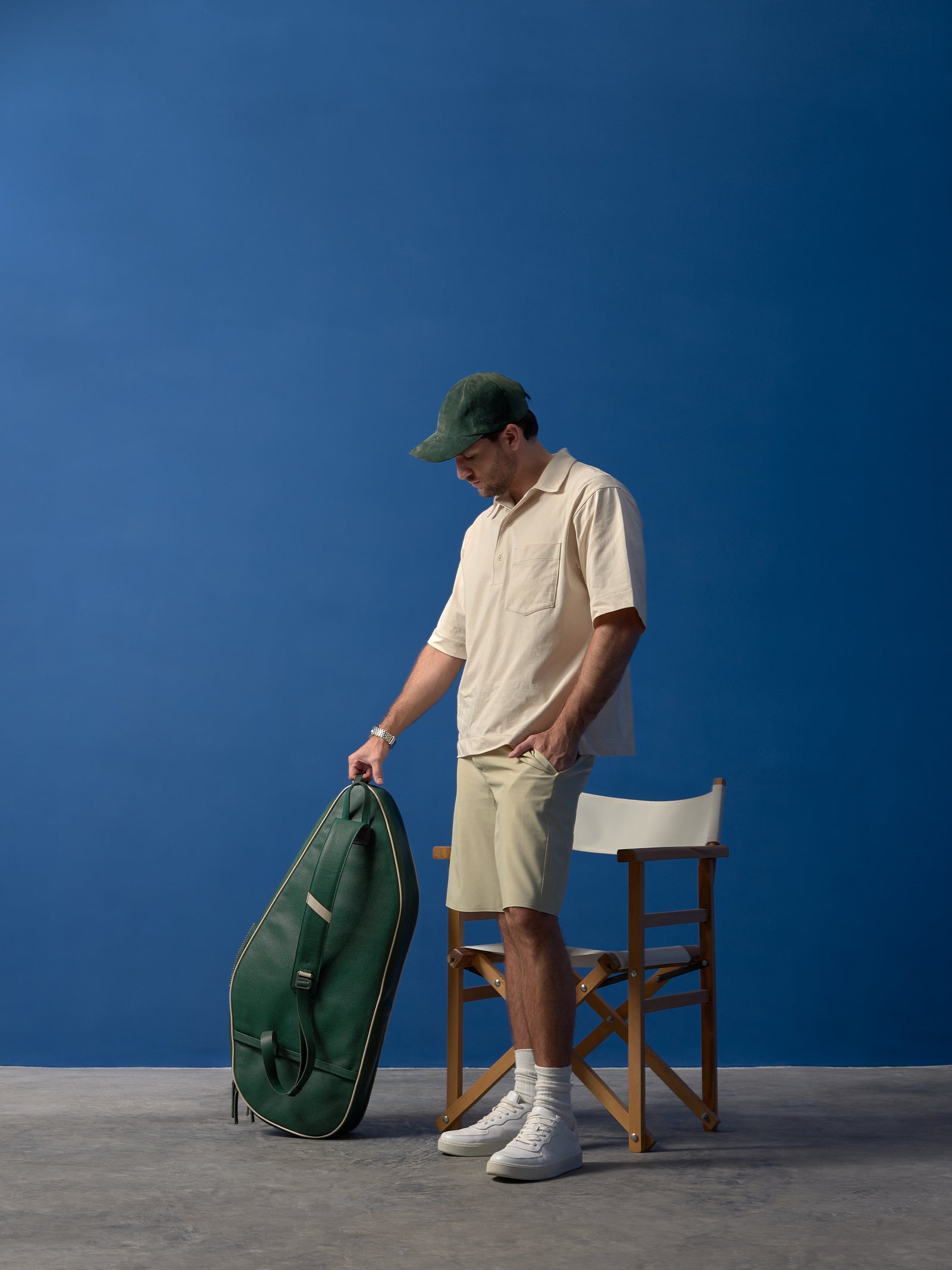 Aesthetic lifestyle shot of a man with a green leather tennis bag standing by a classic director's chair.