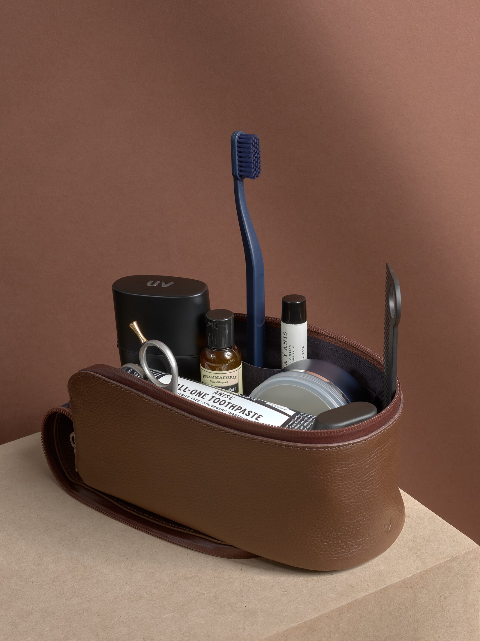 Open brown Capra Leather Toiletry Bag standing, filled with grooming products and accessories.
