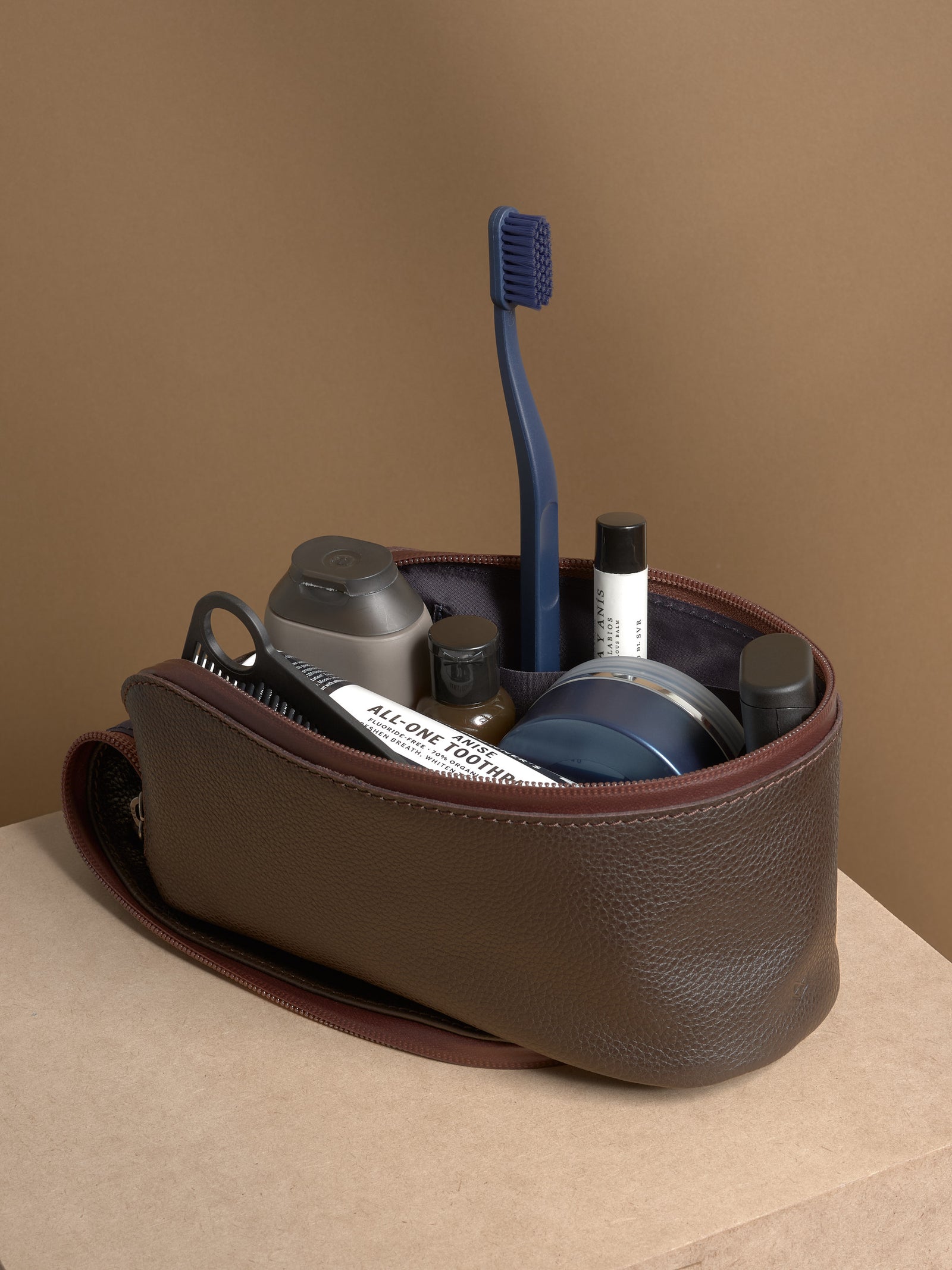Open dark brown Capra Leather Toiletry Bag standing, filled with grooming products and accessories.