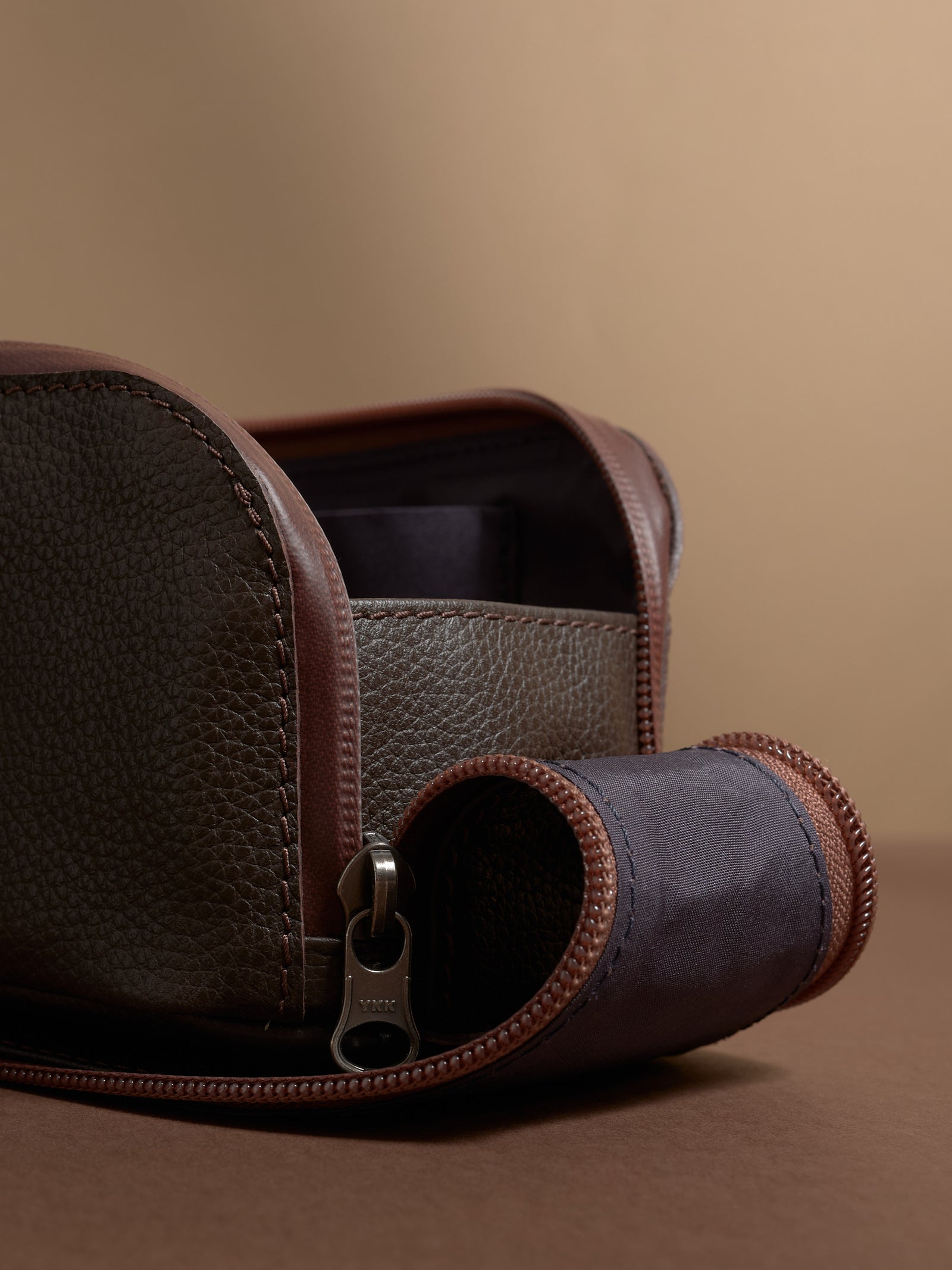 Close-up view of the pebbled dark brown leather, zipper, and construction detail.