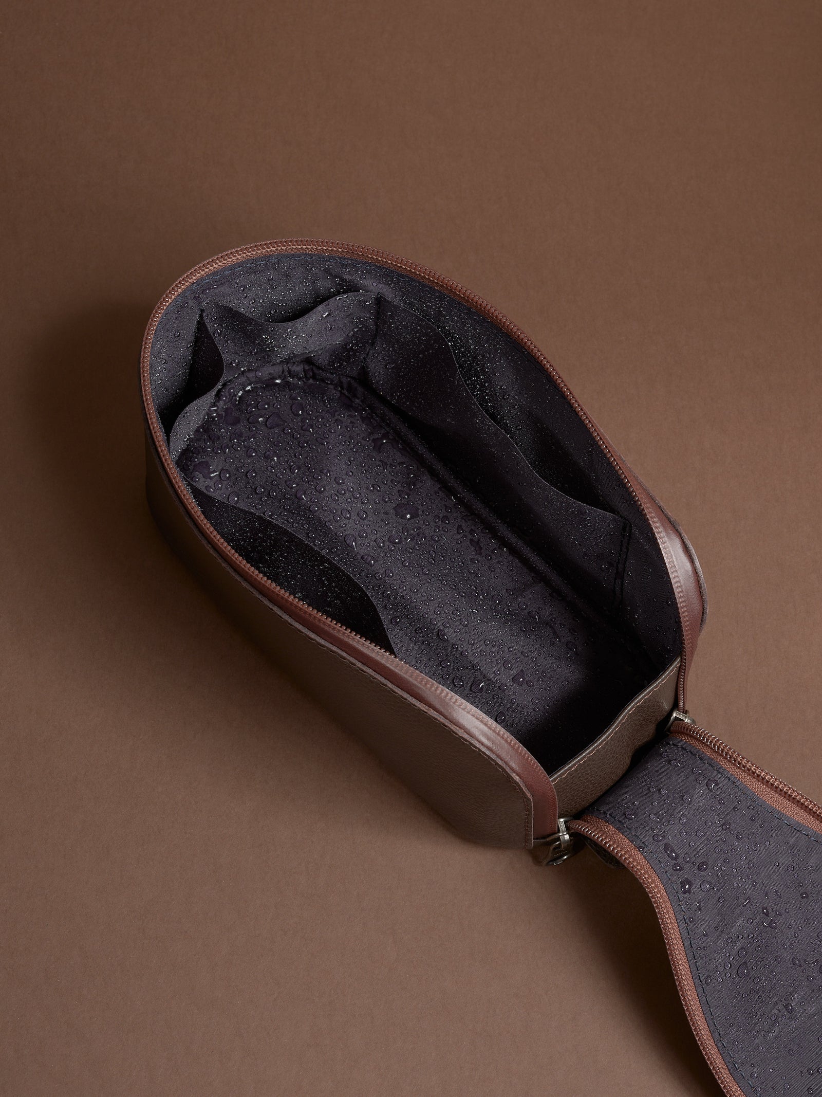 Open dark brown Capra Leather Toiletry Bag showing the water-resistant lining with moisture.