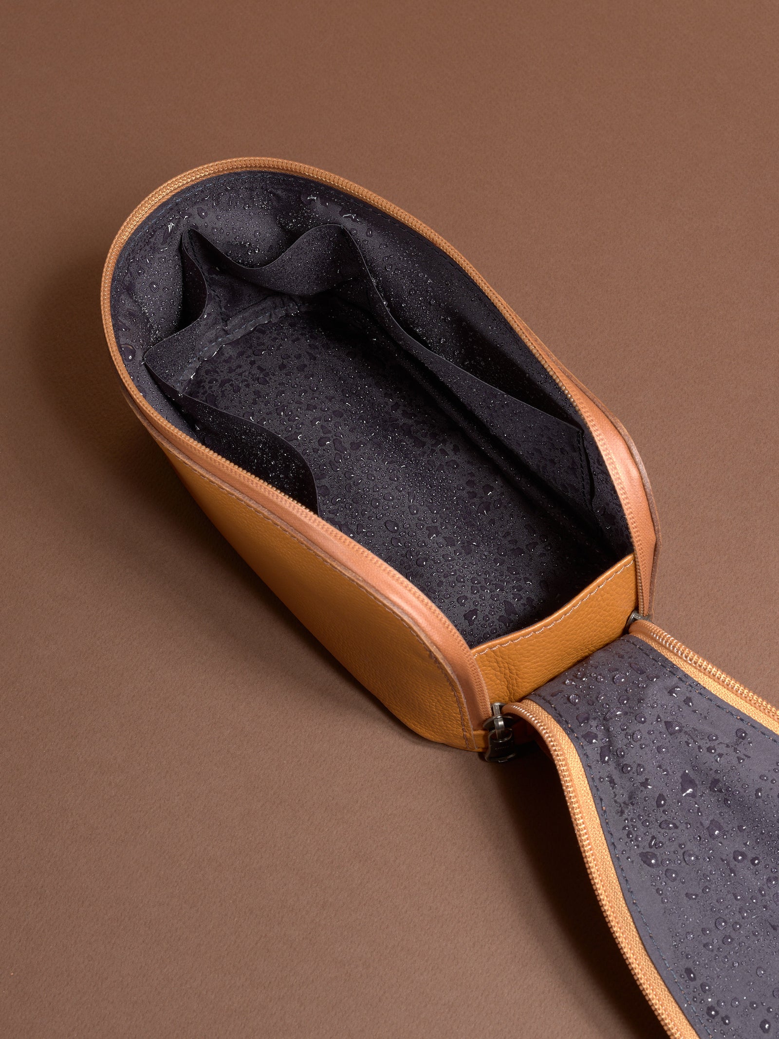 Open tan Capra Leather Scout Toiletry Bag showing the water-resistant lining with moisture droplets.