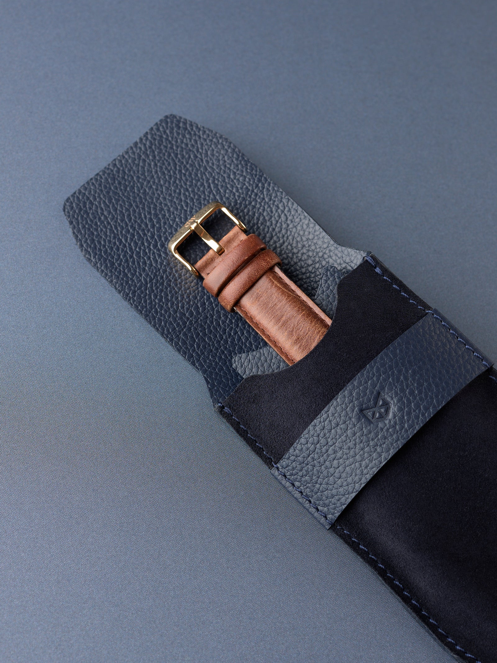 A watch with a brown leather strap sliding into the protective navy suede interior of the Capra Leather watch pouch.