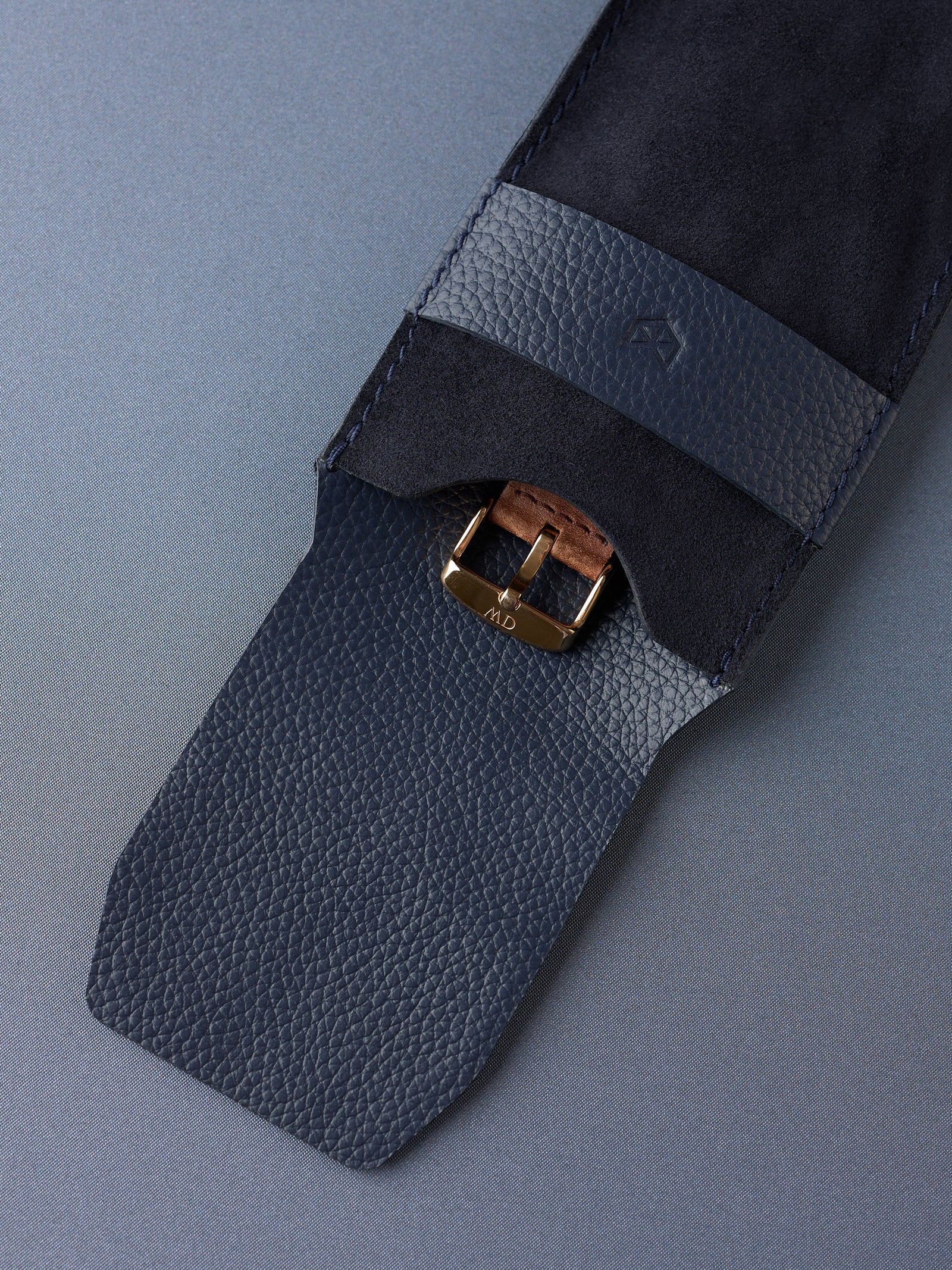 Detail shot of a watch buckle securely held under the navy pebbled leather strap of the Suede Watch Pouch.