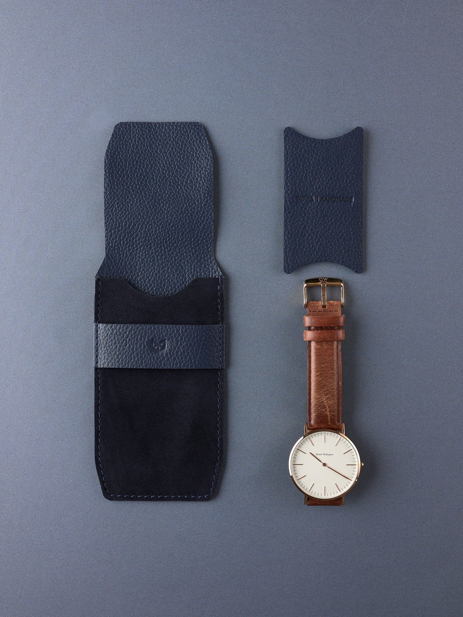 A flat lay of the Capra Leather navy suede watch pouch, its separate leather insert, and a minimalist gold watch.