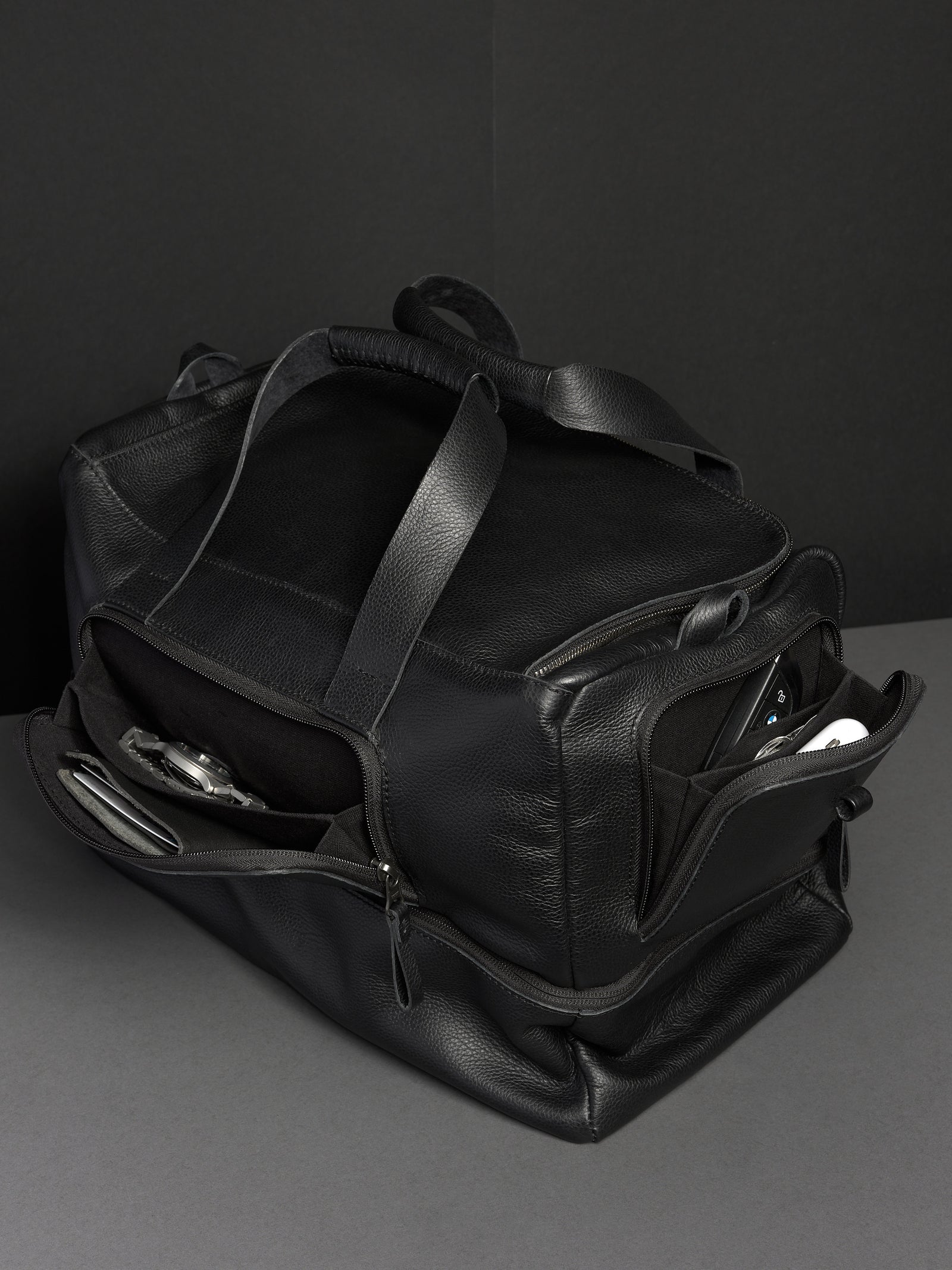 Black leather duffel bag, unzipped to reveal spacious interior and multiple side pockets for organization.