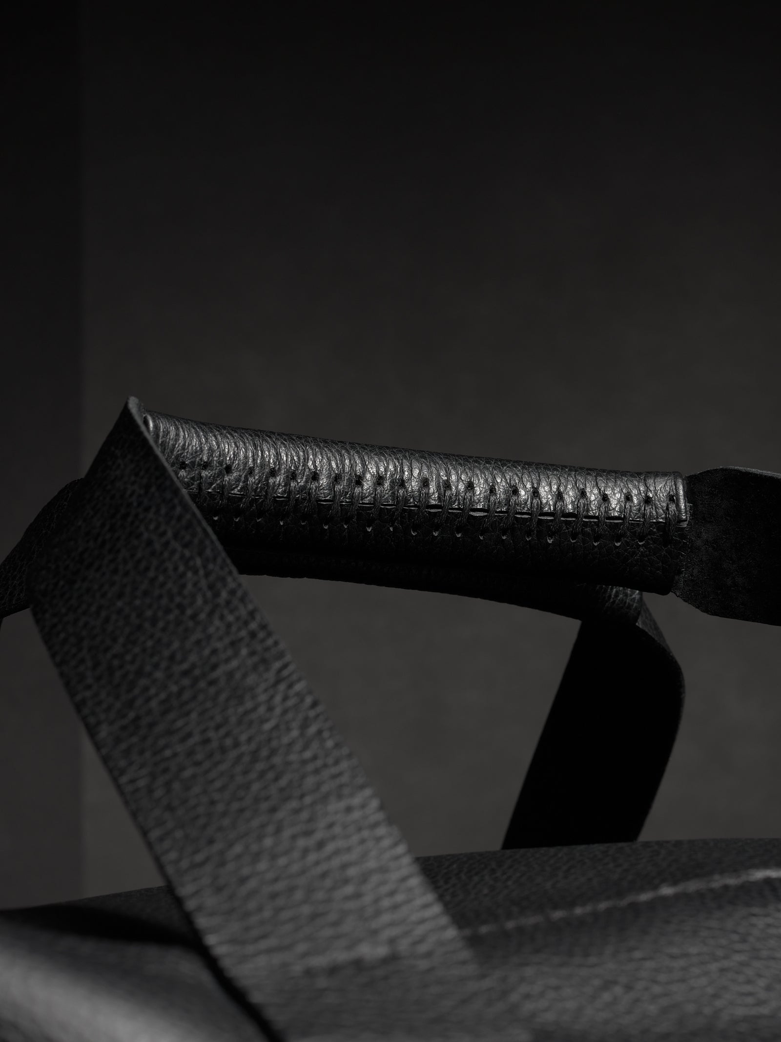 Close-up of the black leather handle of the Ventra duffel, highlighting the detailed stitching and pebbled texture.