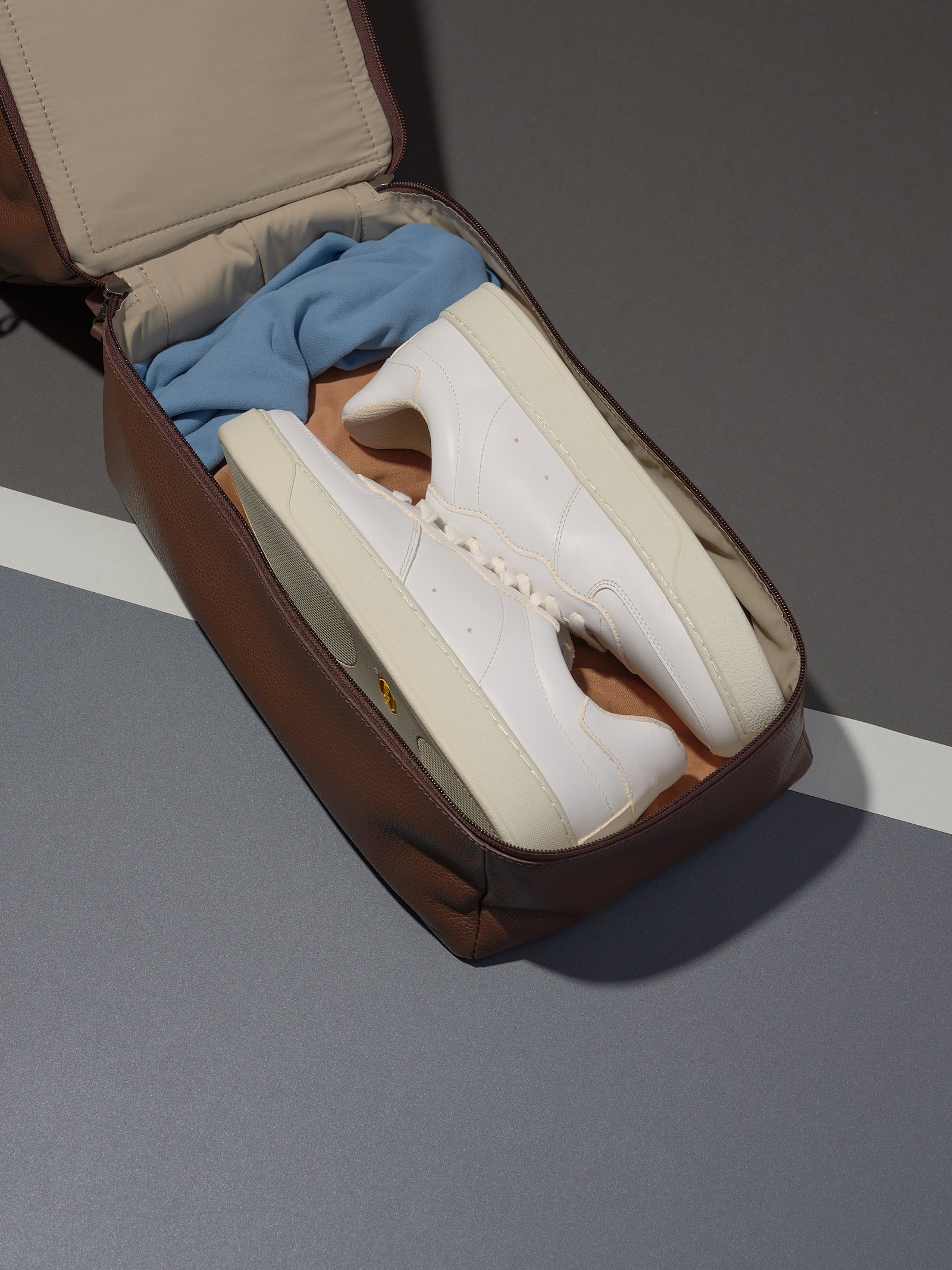 The Ventra Holdall's separate shoe compartment in brown leather, open to hold a pair of white sneakers for the gym.