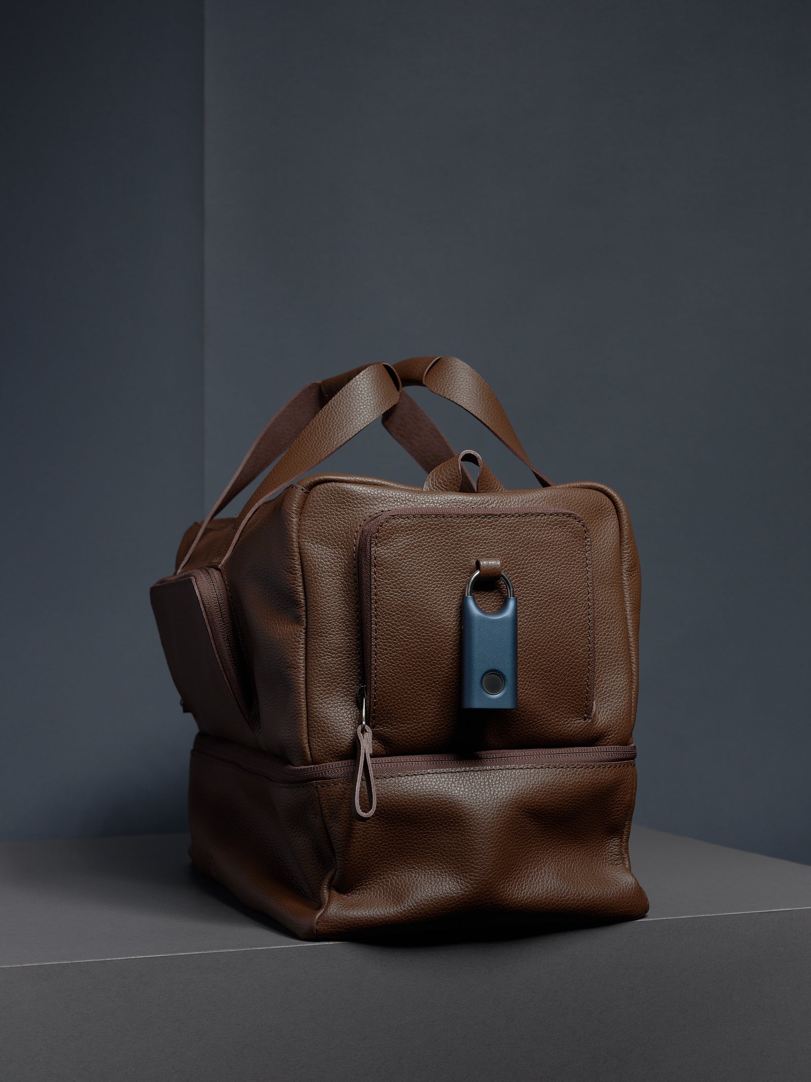 Front of the brown leather Ventra Holdall, showcasing a blue smart tracker attached to the dedicated security loop.