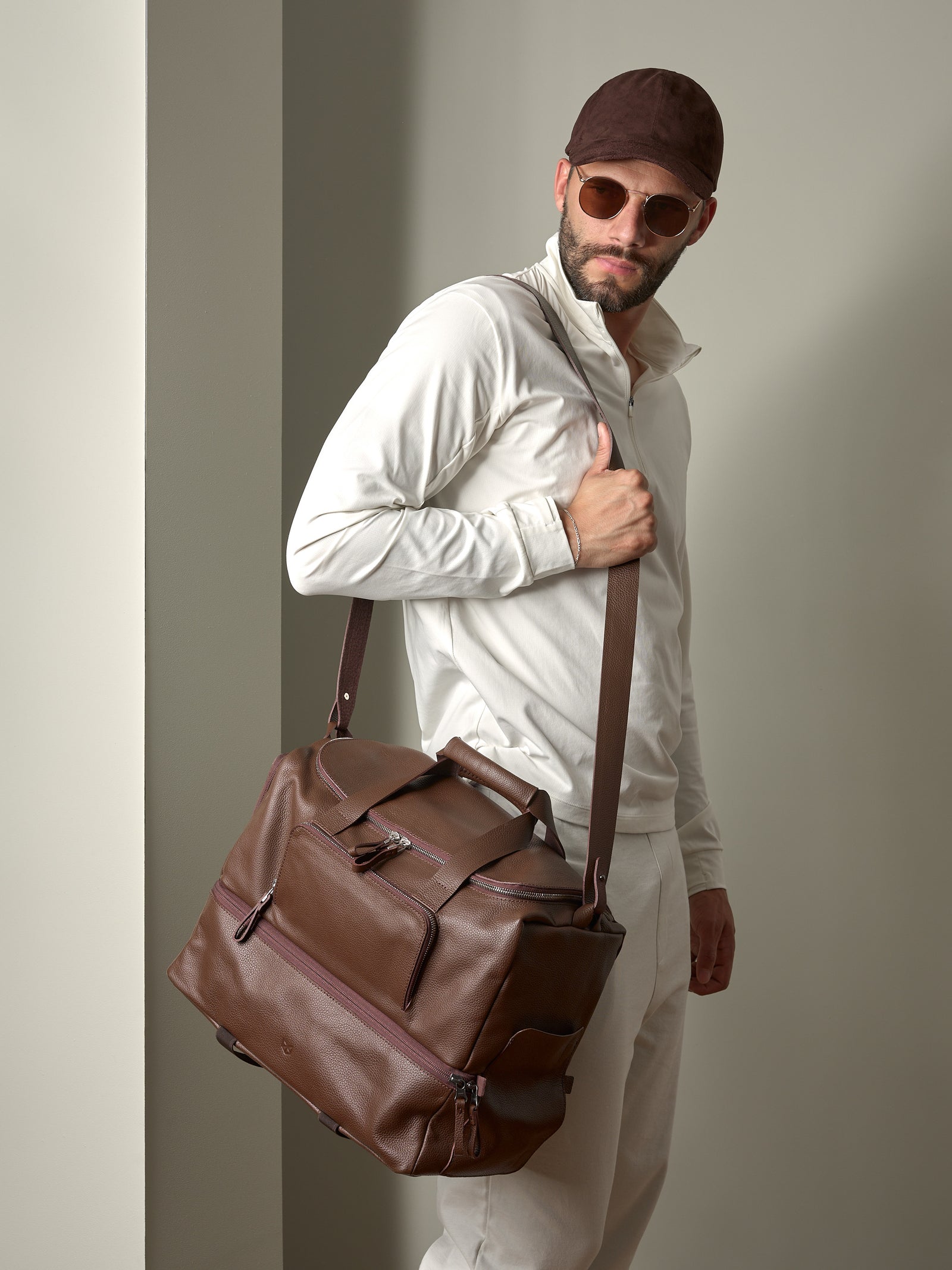 A stylish man carrying the brown leather Ventra Holdall over his shoulder using the comfortable, long strap.