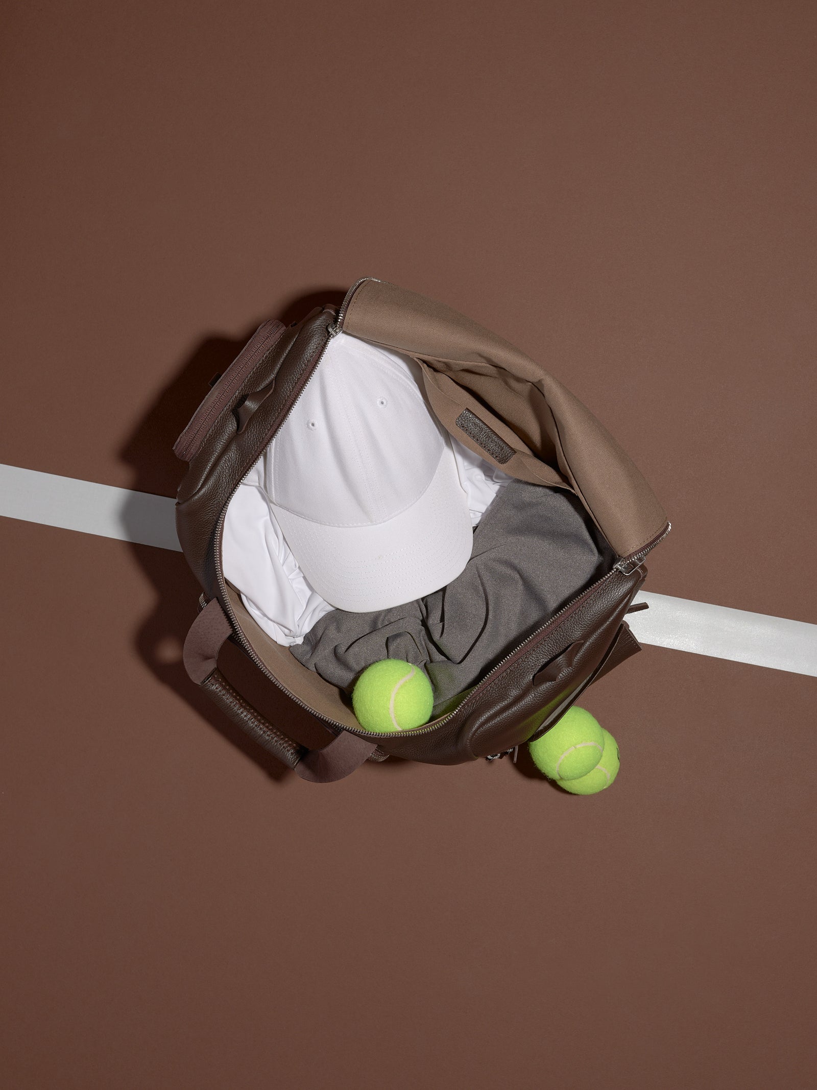 A Ventra Holdall bag opened from the top, holding a white hat and grey shirt with two tennis balls next to it.