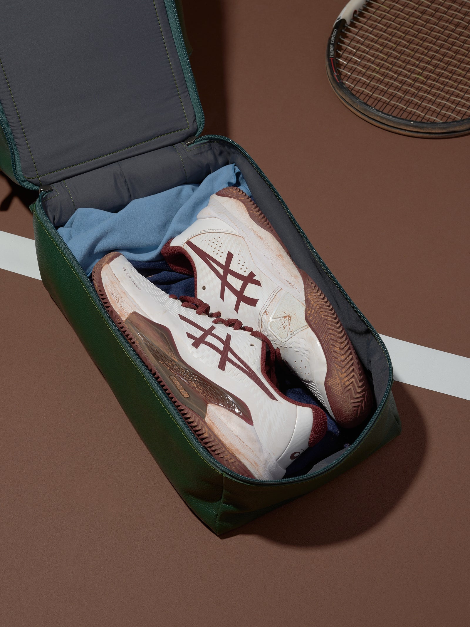A top-down shot of the green leather Ventra Holdall on a tennis court, positioned as a luxury men's sports bag.