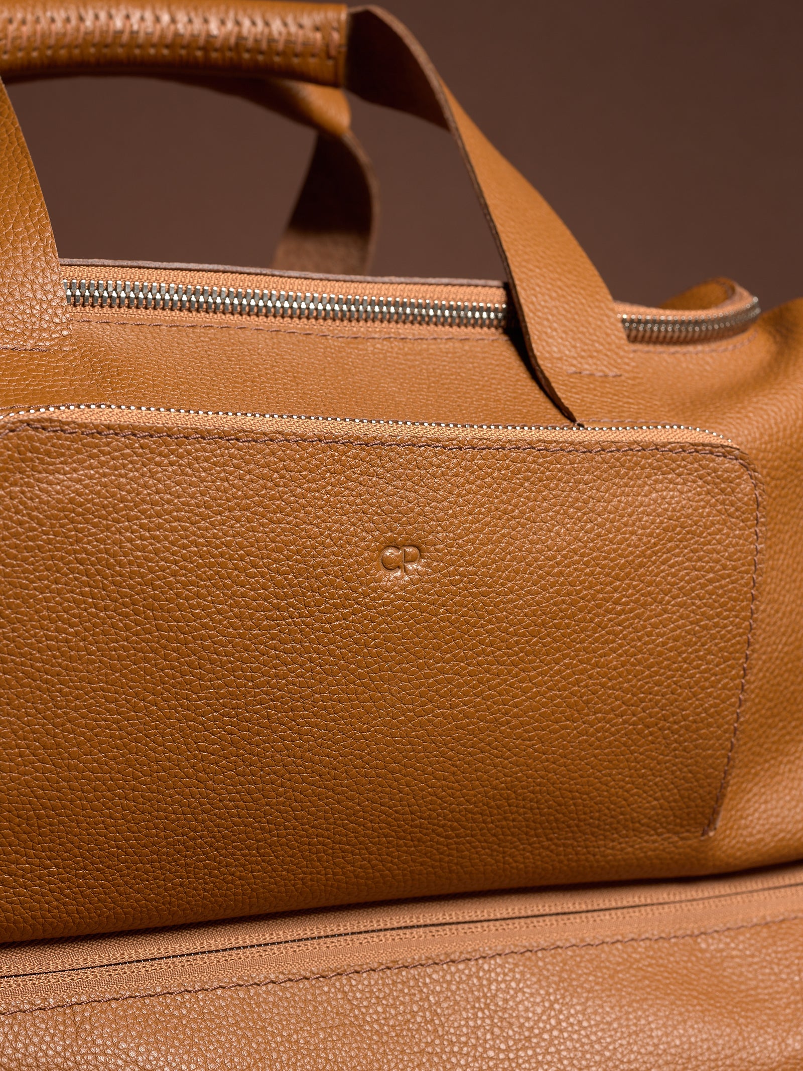 Close-up of the custom debossing in the full-grain leather texture, zipper, and subtle Capra Leather logo on the exterior pocket of a Ventra Holdall duffel bag.