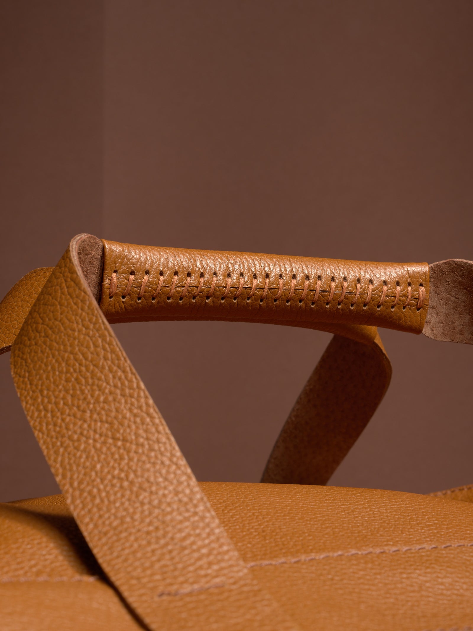 A detailed close-up of the Ventra Holdall's handle, highlighting the intricate hand-stitching on the tan leather grip.
