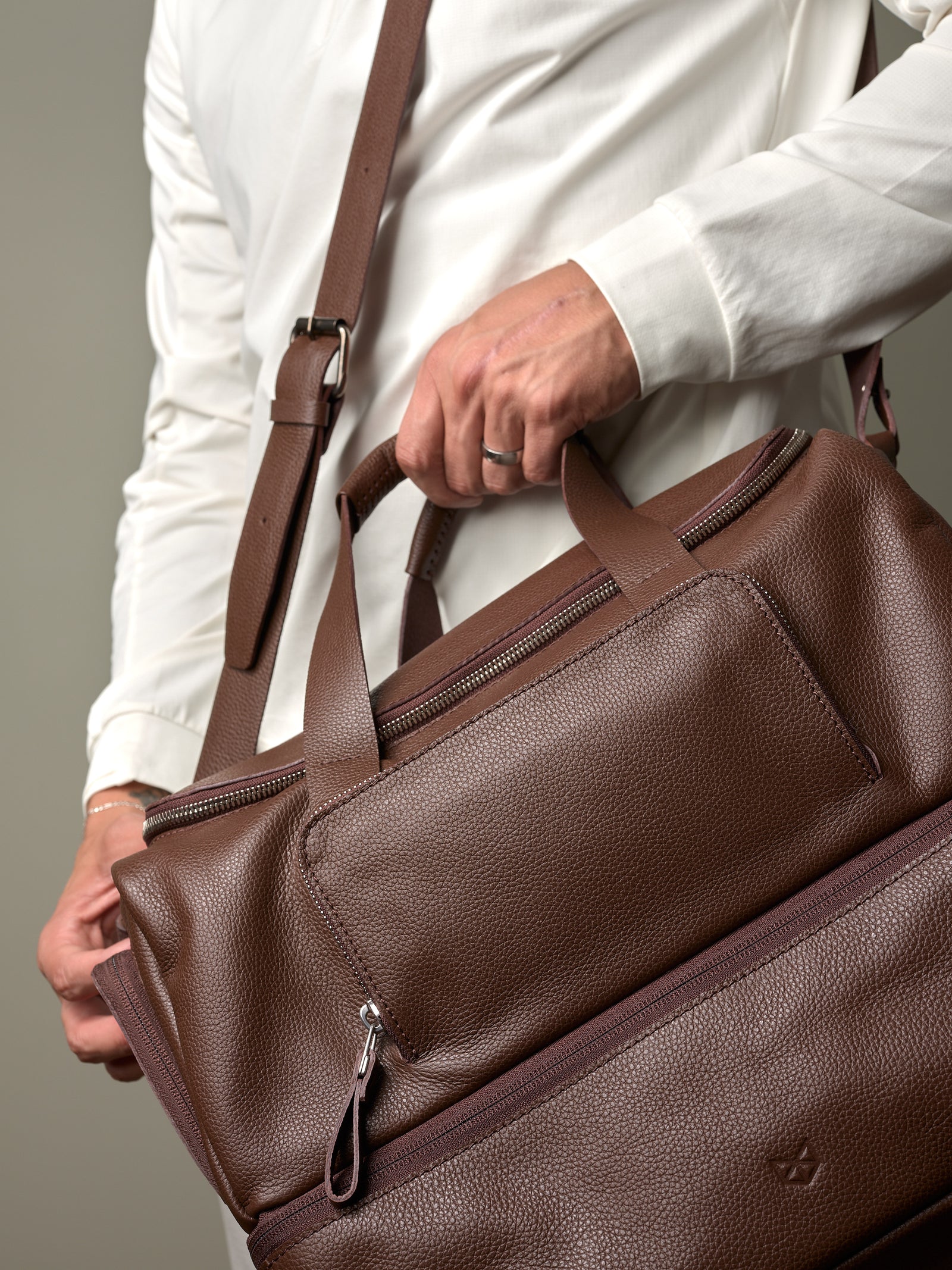 Close-up of a man's hands holding the brown leather Capra Ventra Holdall, highlighting the rich texture and zippered pockets.