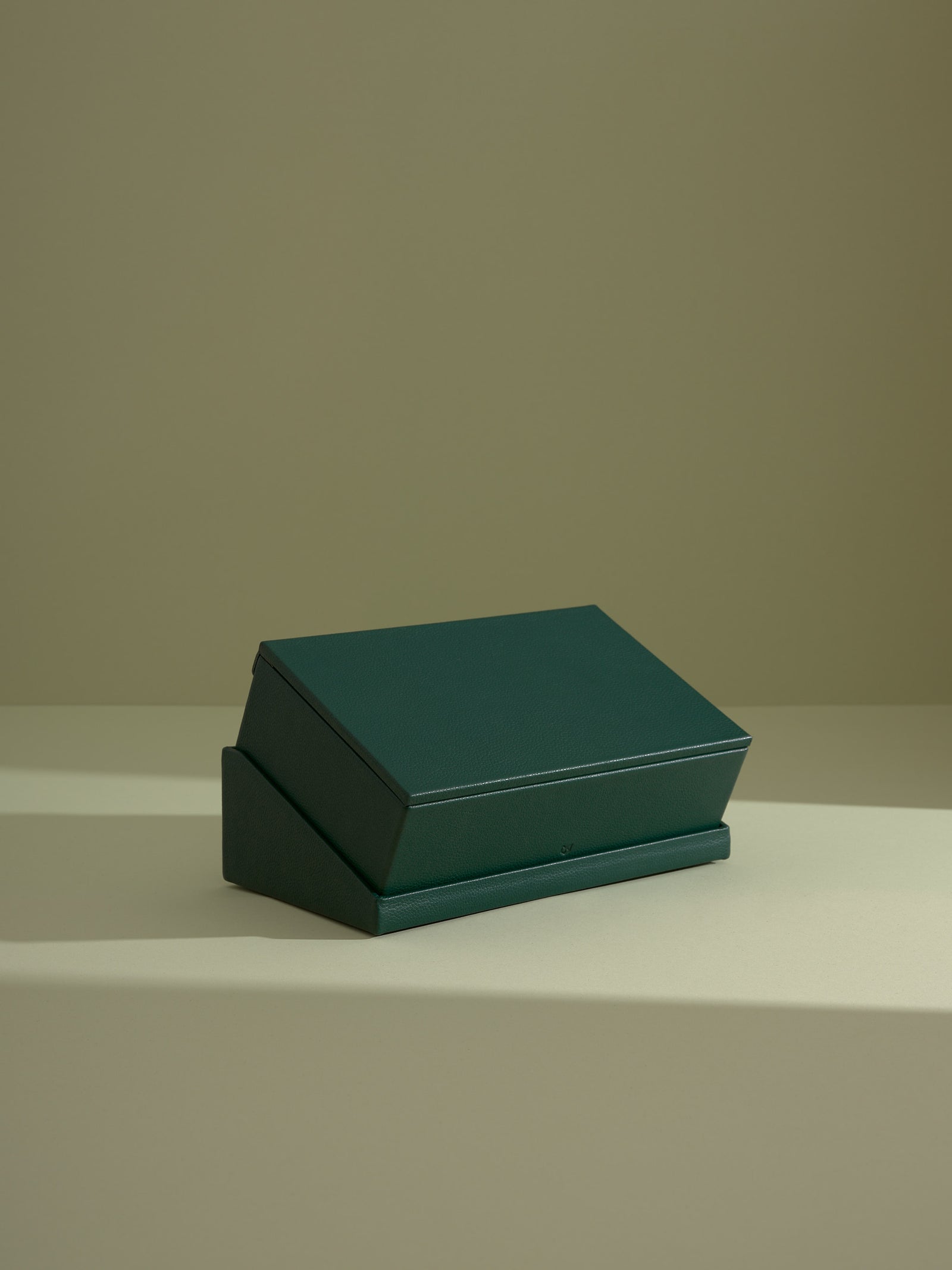 Closed green full-grain leather Podium Watch Box resting on a matching angled display stand base.