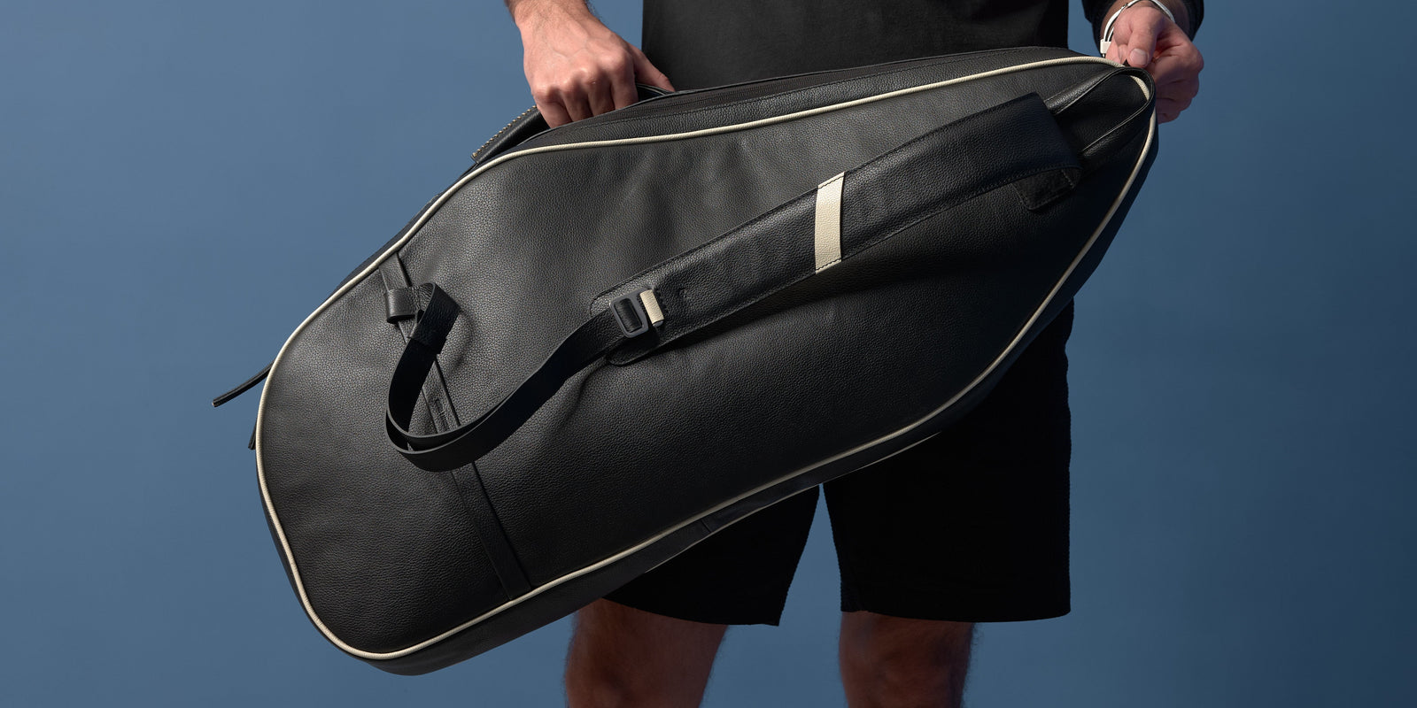 Close-up of a man carrying a black full-grain leather tennis bag.