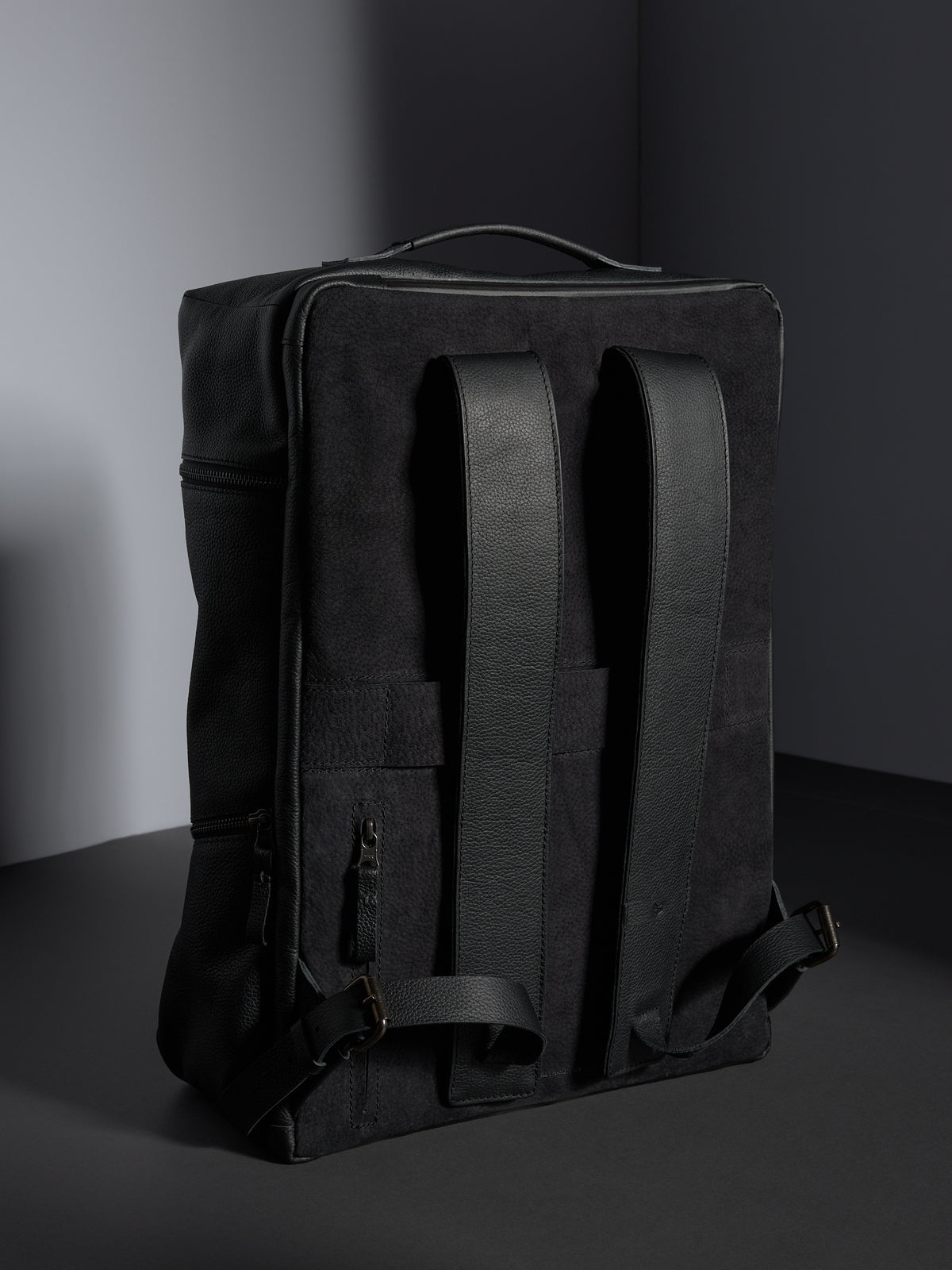 Back view of the black leather backpack showing the cushioned straps and premium suede-like backing for comfort.