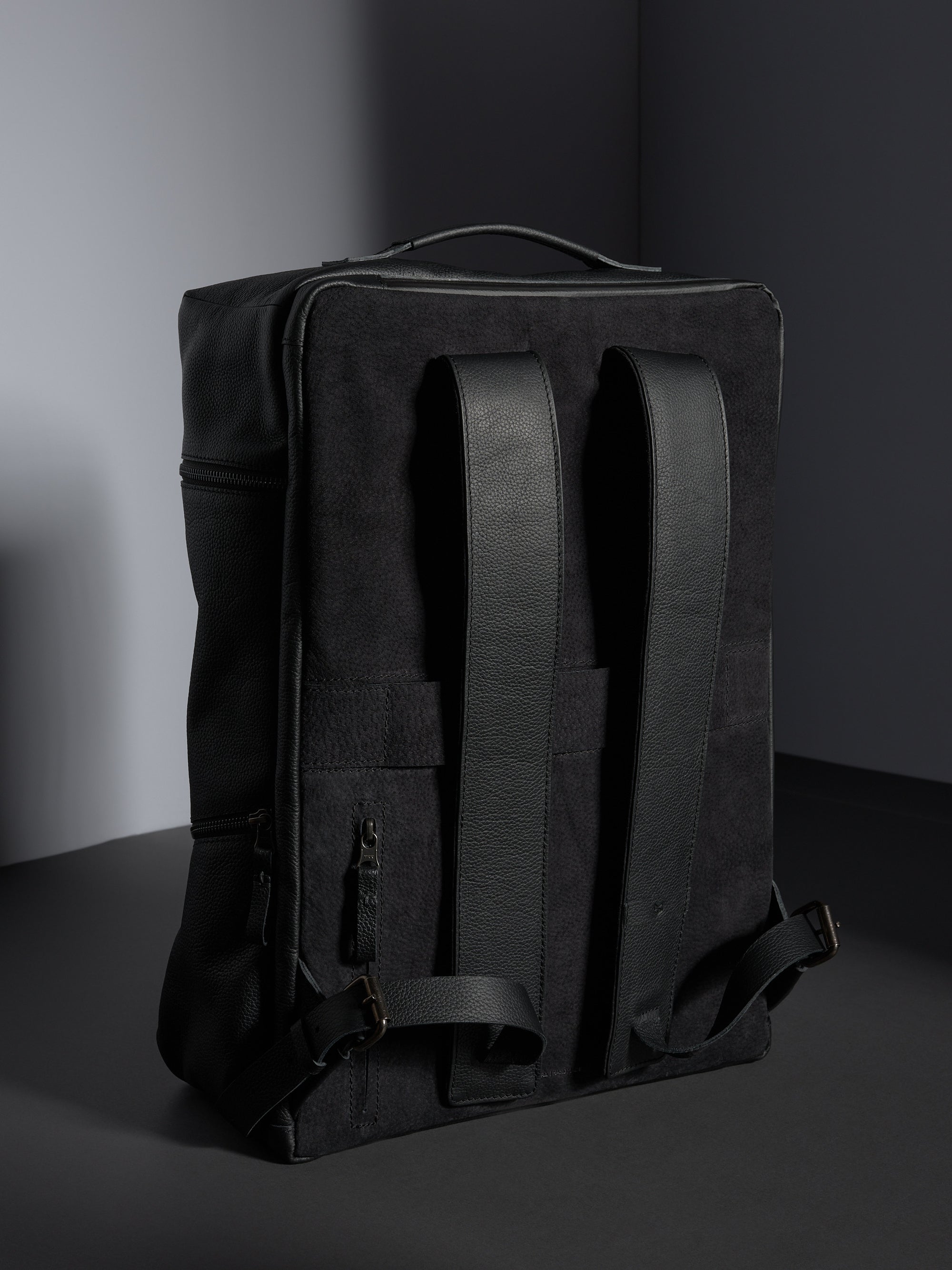Back view of the black leather backpack showing the cushioned straps and premium suede-like backing for comfort.