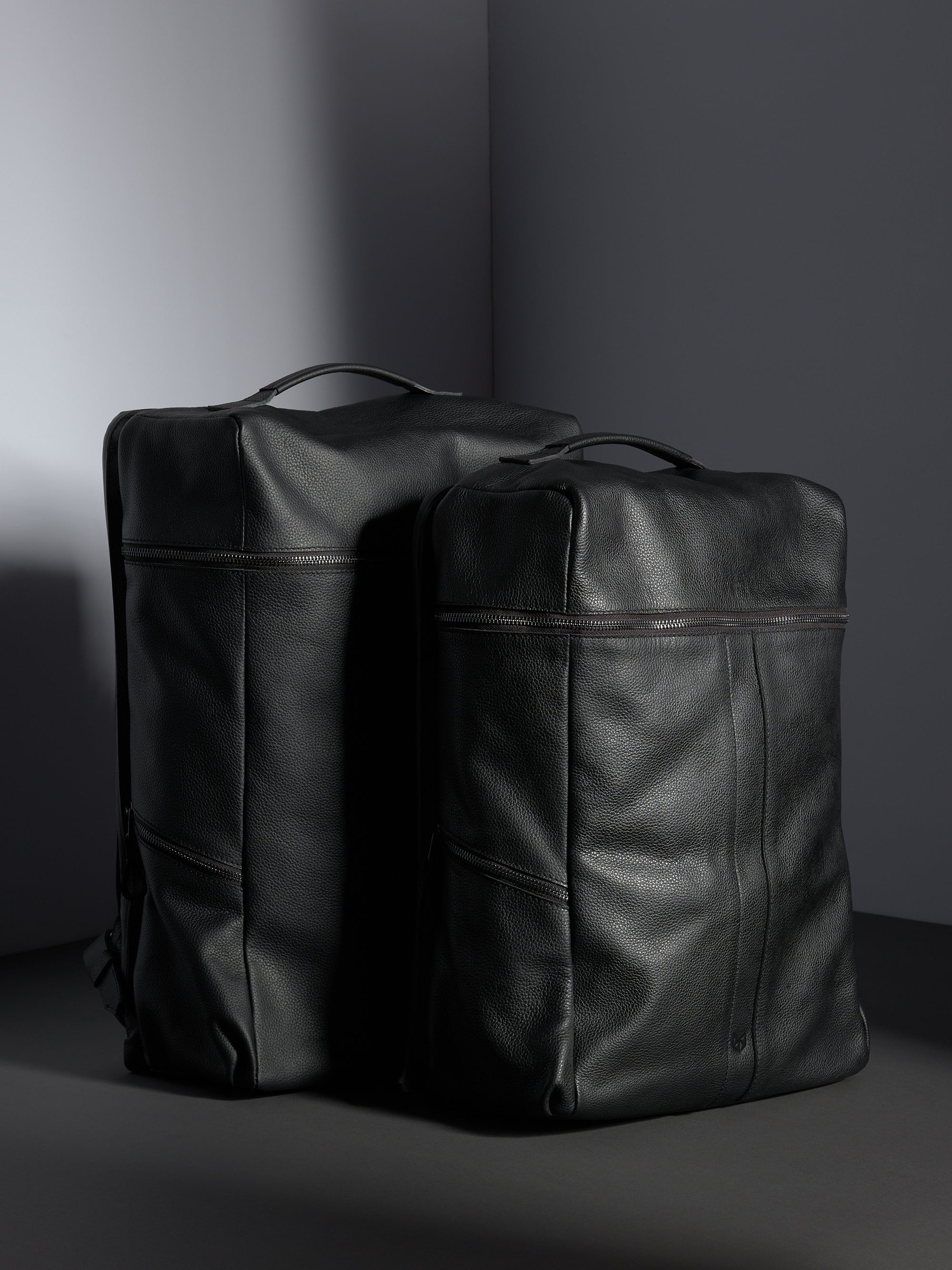The large and smaller sizes of the Banteng black full-grain leather backpacks standing side-by-side.