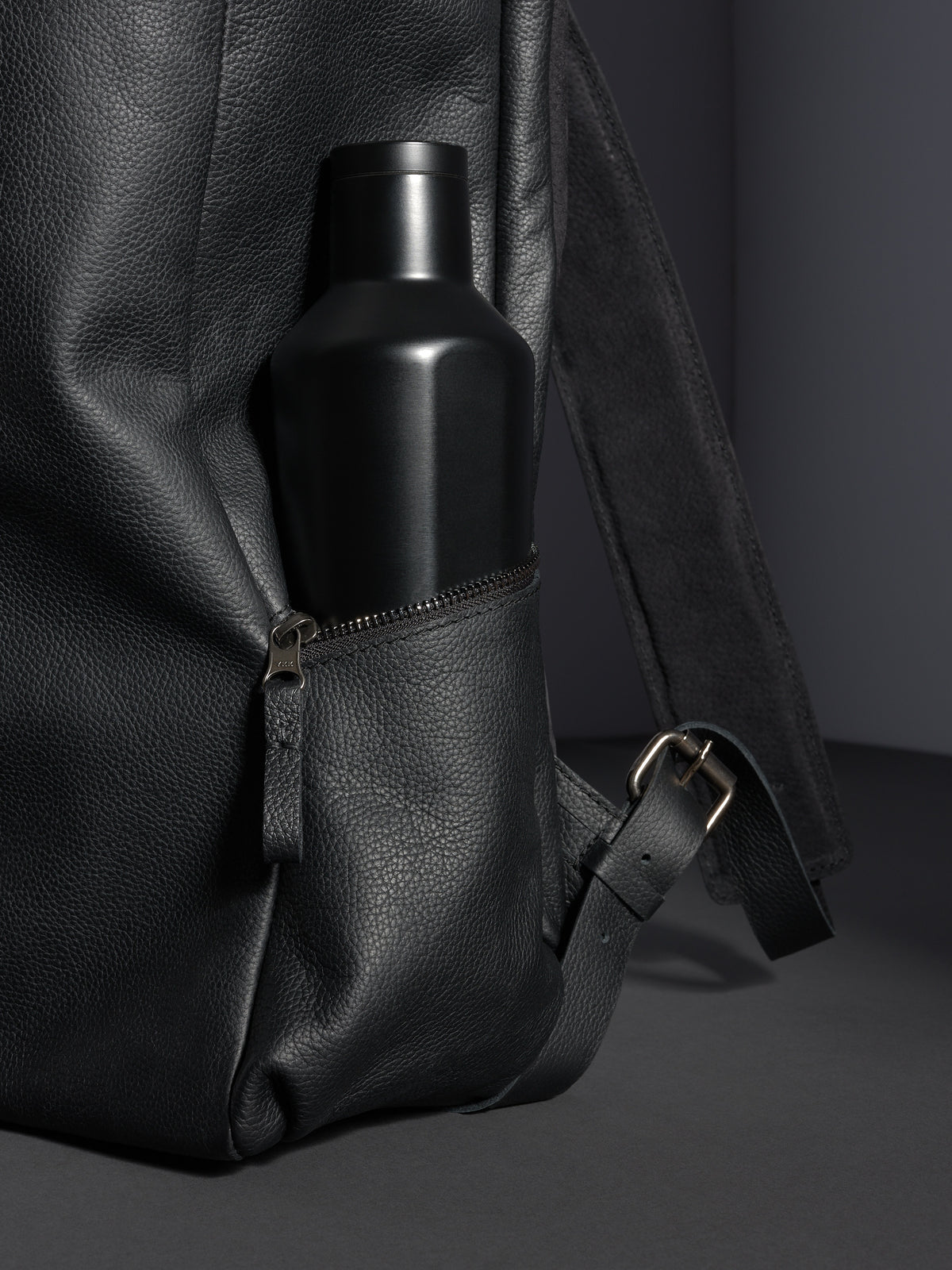 Black Capra Leather backpack's zippered side pocket with a matte black water bottle inserted.