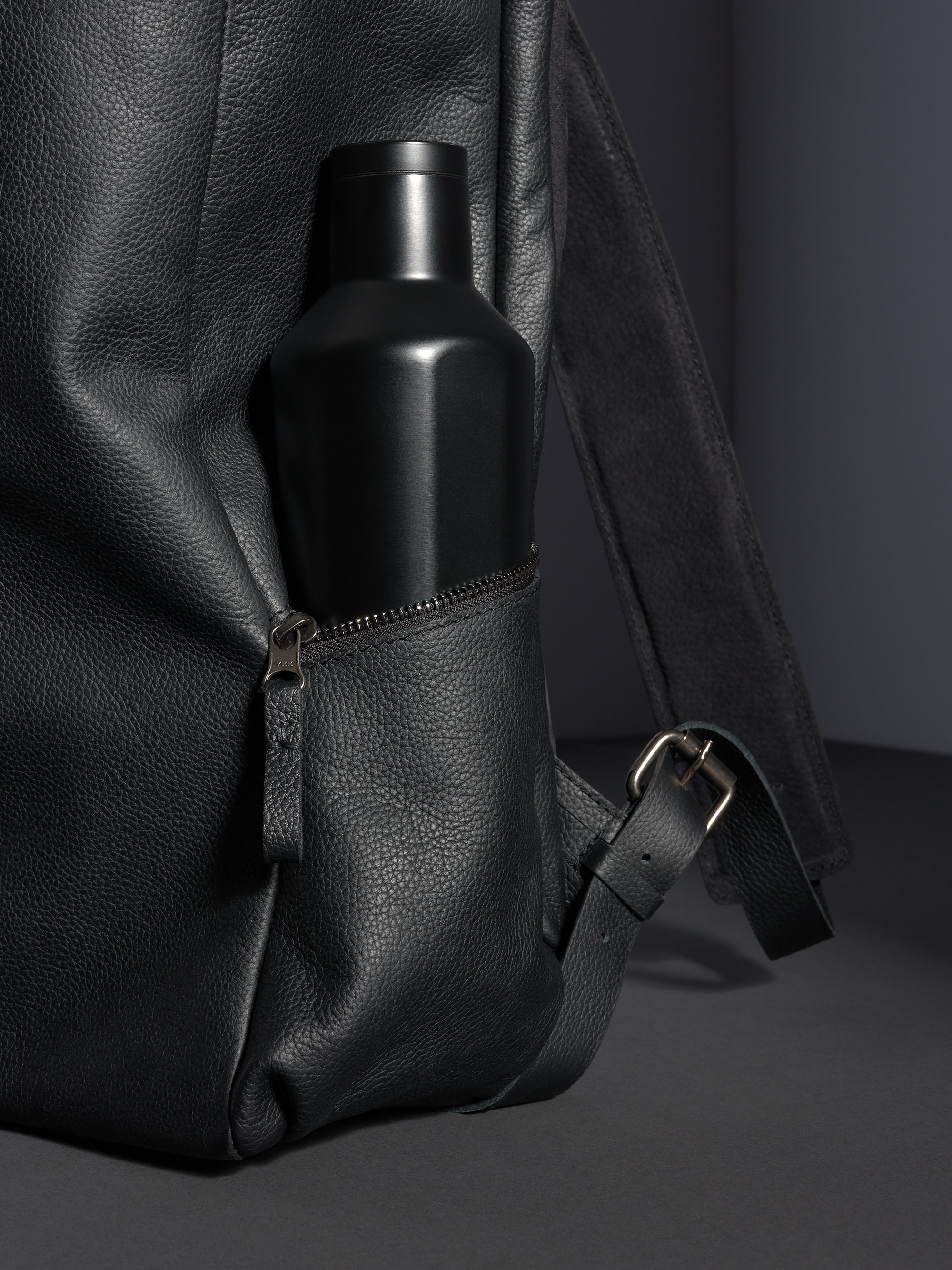 Black Capra Leather backpack's zippered side pocket with a matte black water bottle inserted.